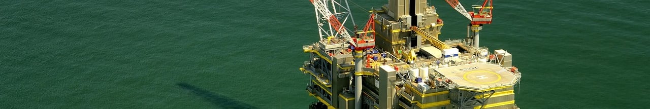 Vista aérea de uma plataforma petrolífera marítima e um navio de abastecimento ao lado.