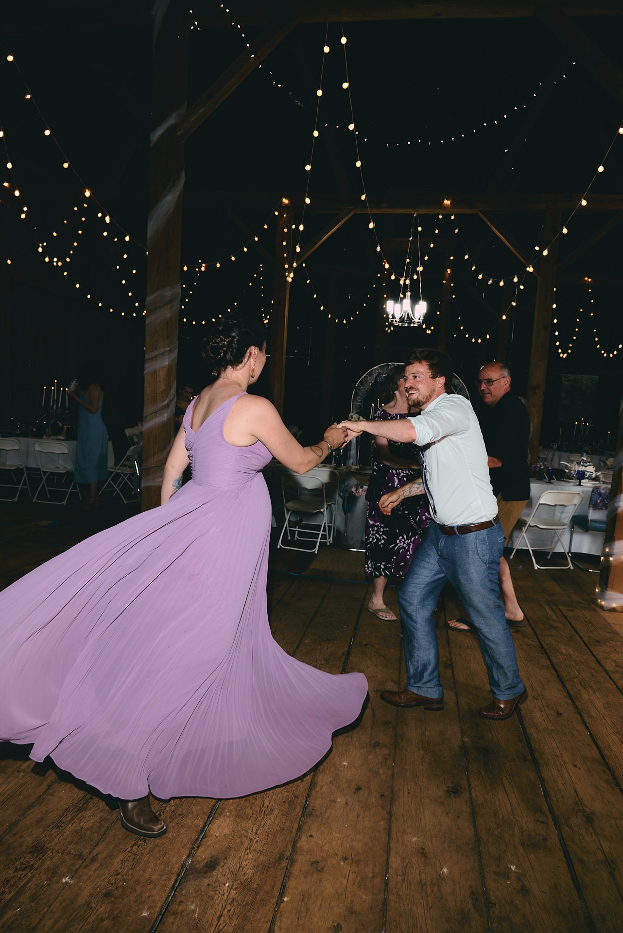 a man and woman in a purple dress dancing at a wedding reception in a barn