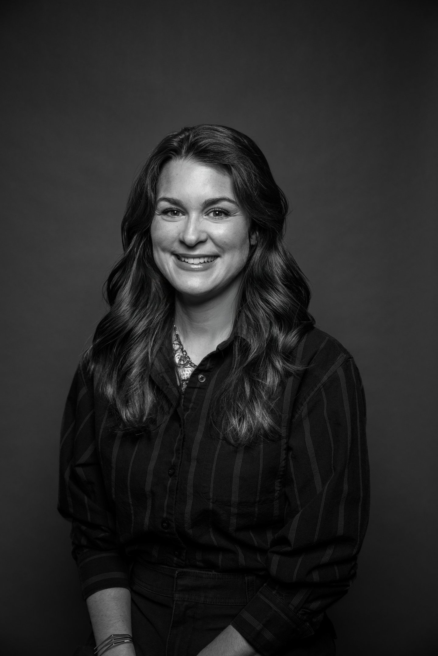 Portrait professionnel en noir et blanc d’une femme souriante aux longs cheveux ondulés 