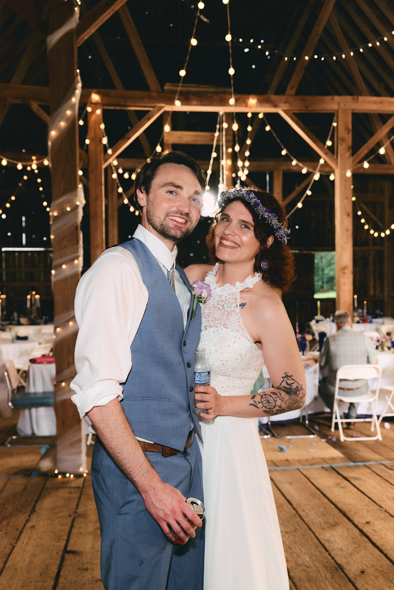 a grrom and bride holding each other and standing in a barn with lights in the background