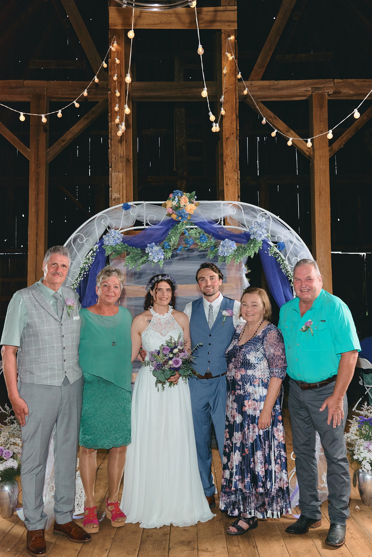 a family wedding picture with a bride and groom in front of wedding arch in a barn