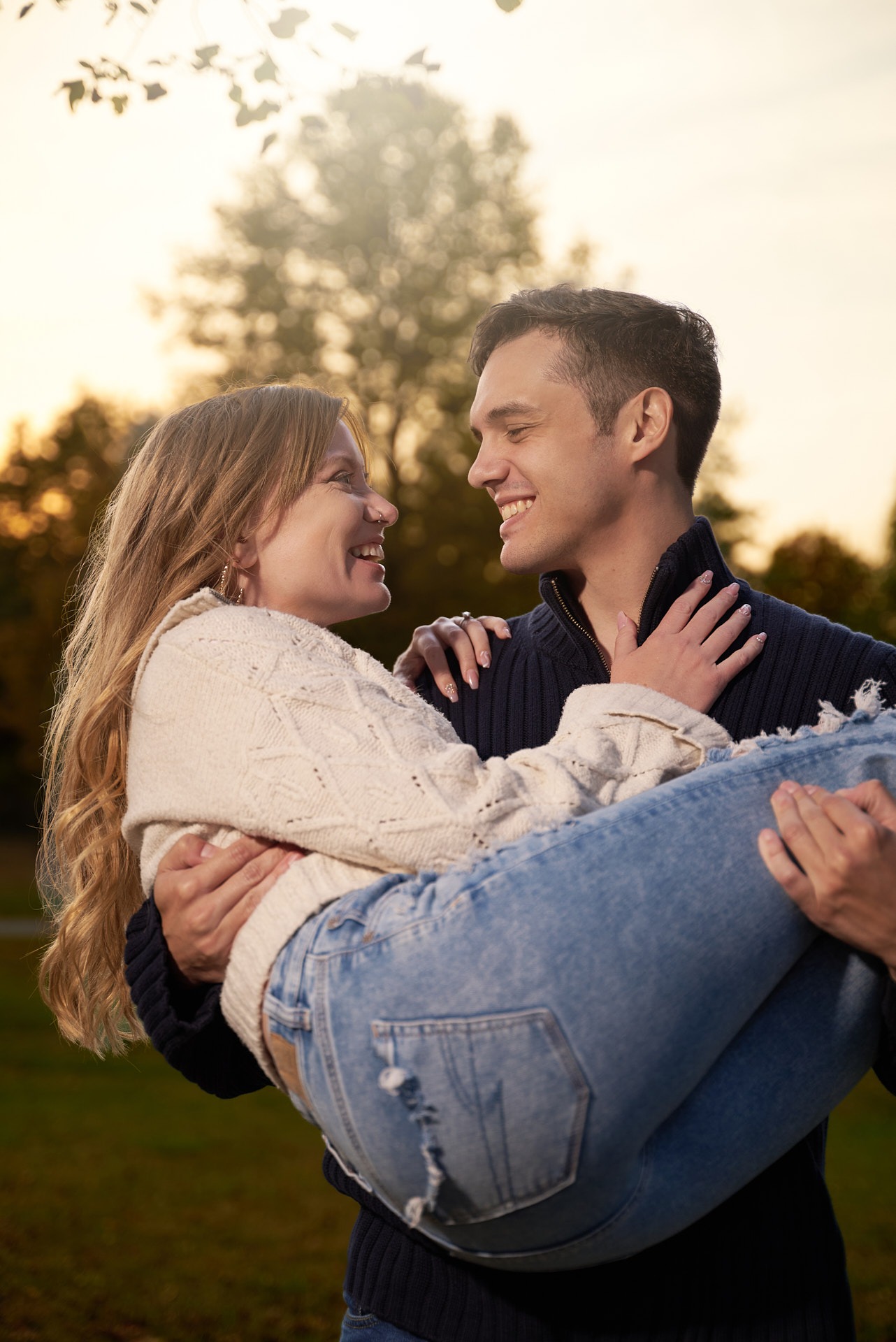 a man carring a woman in his arms in front of a tree and sunset