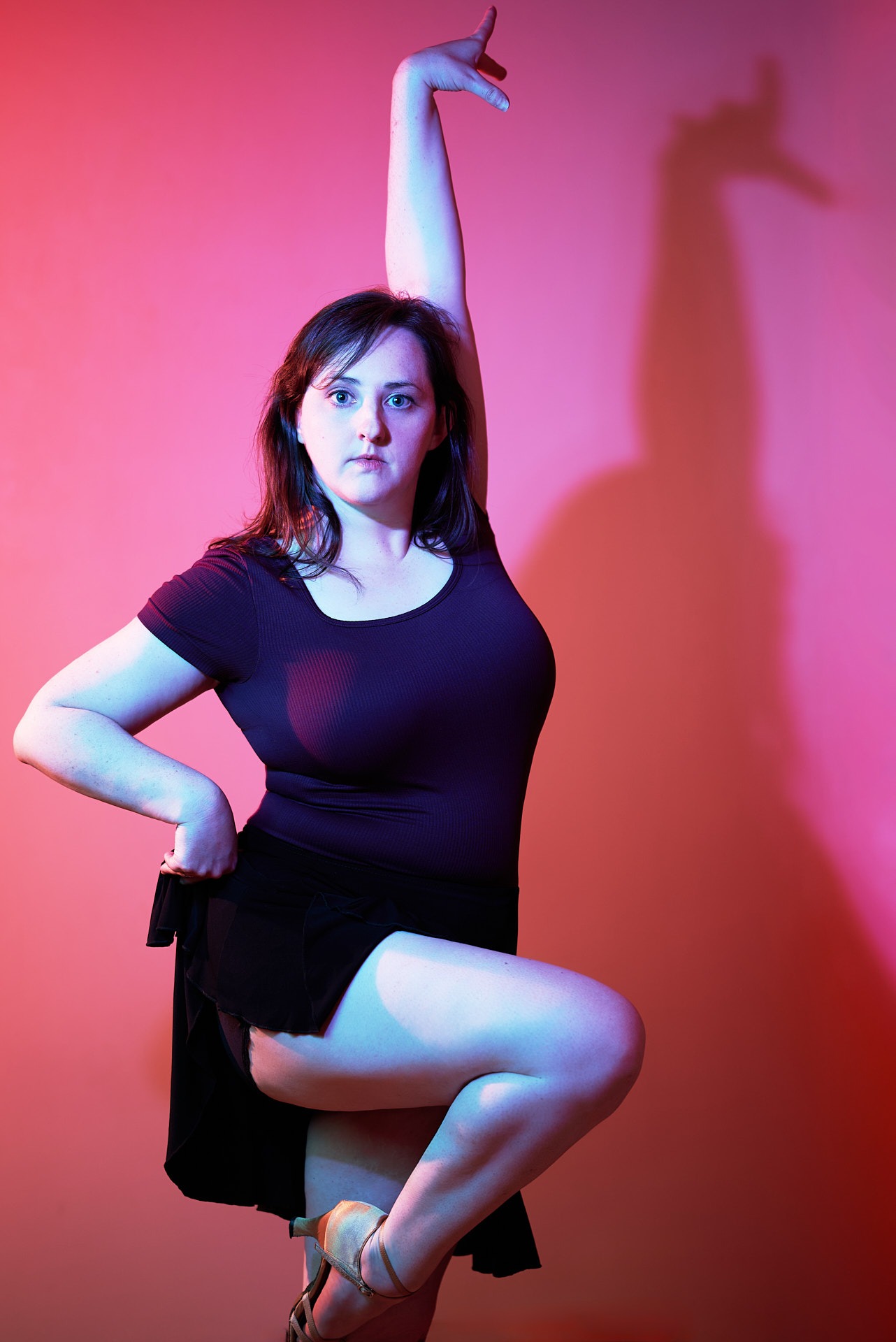 a woman in a black dress and heels is posing as a dancer in front of pink background