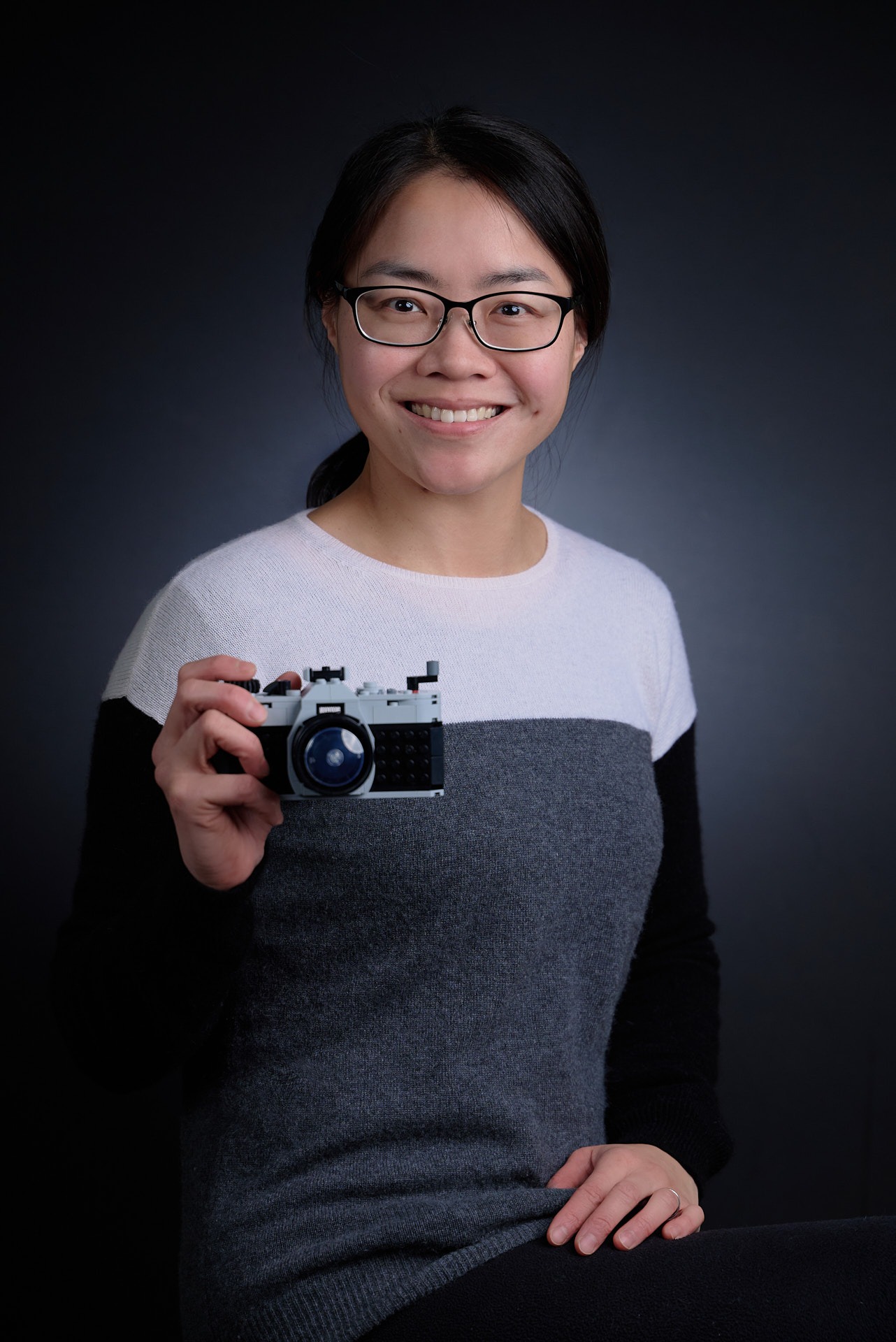 a woman in glasses and a sweater holding a lego camera