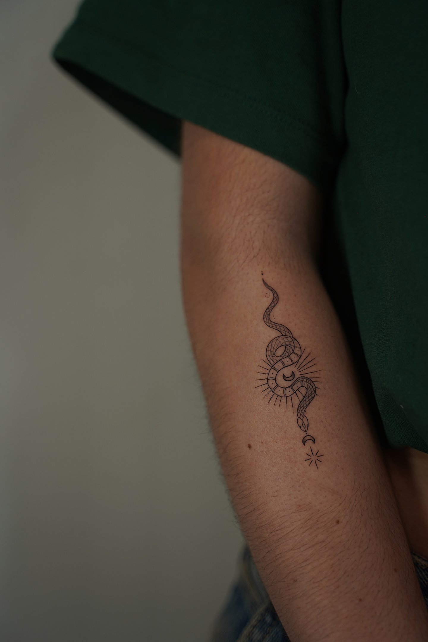 Tatuaje fineline en Madrid de serpiente mística enroscada en sol radiante con luna creciente