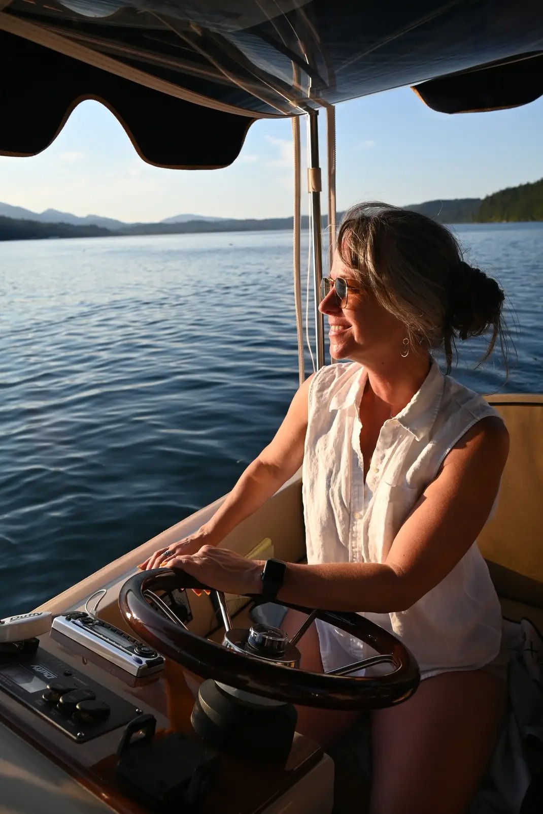 a beautiful woman in a white shirt is sitting on a eco-friendly electric boat cruising hood canal