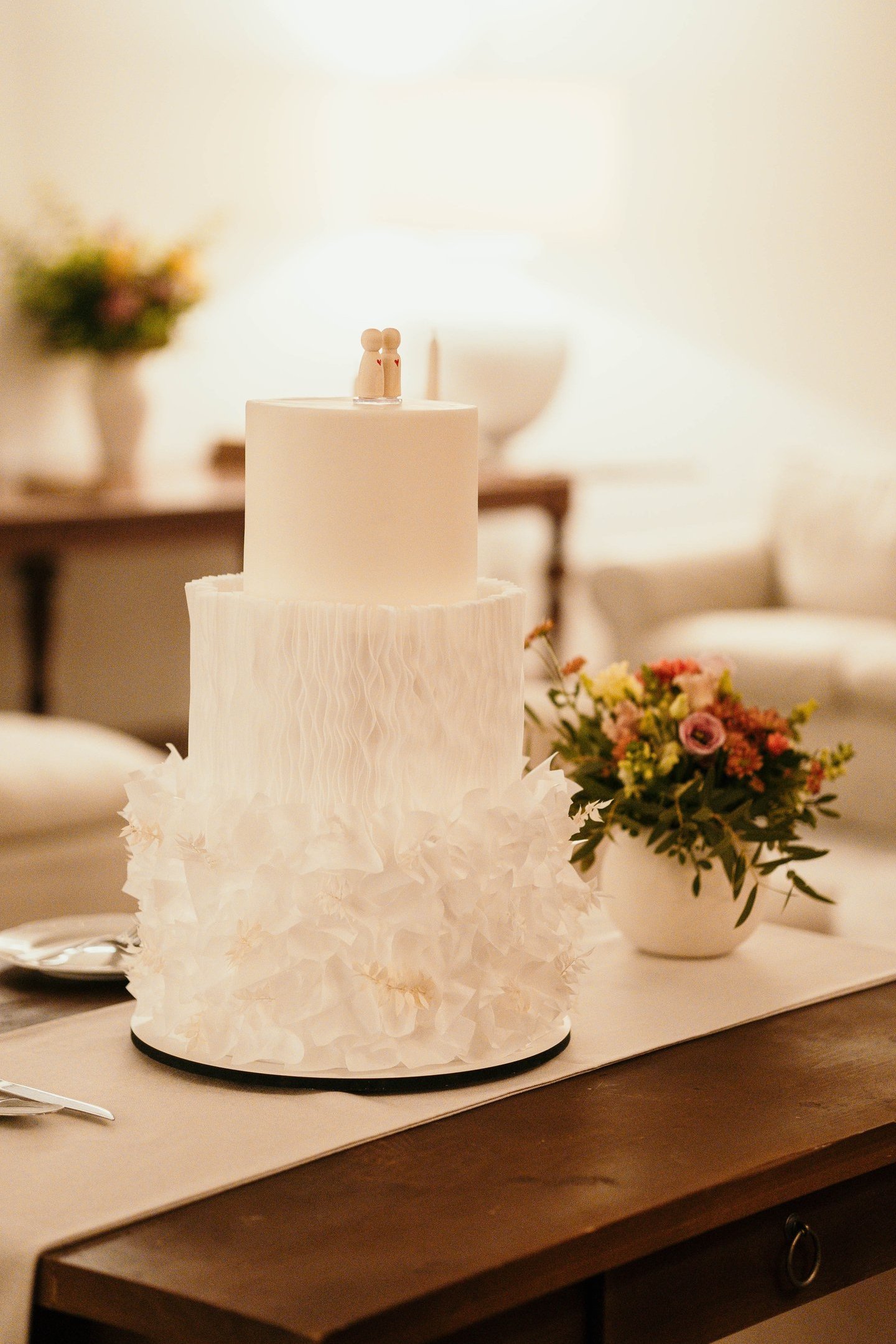 Elegant three-tier white wedding cake with textured ruffles and a minimalist peg doll topper.