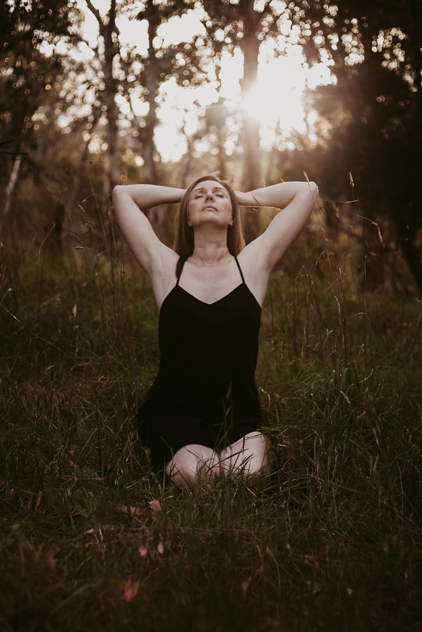 a woman in a black bathingsuit sitting on the grass