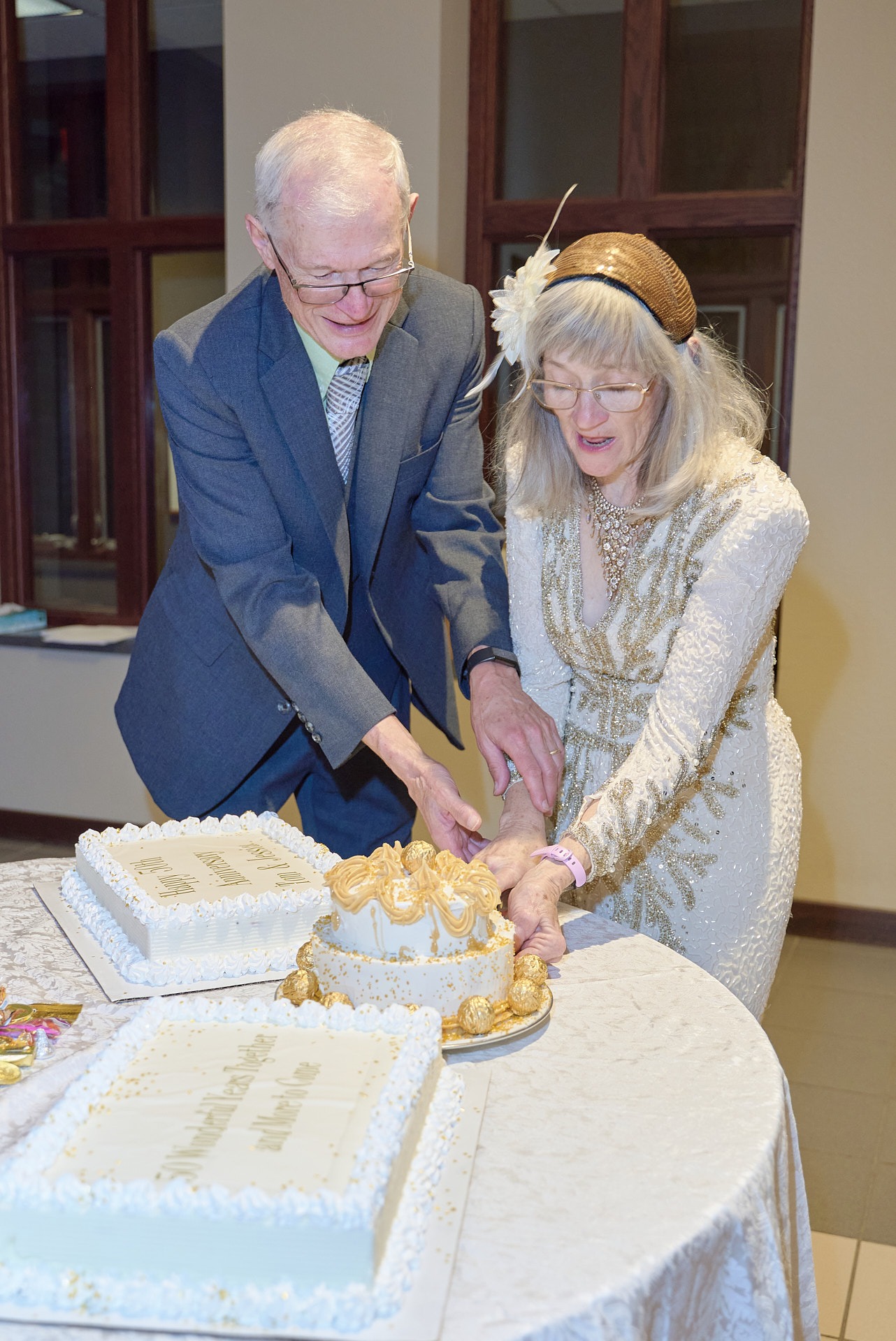 A senior couple celebrates their 50th wedding anniversary cutting a gold and white cake.