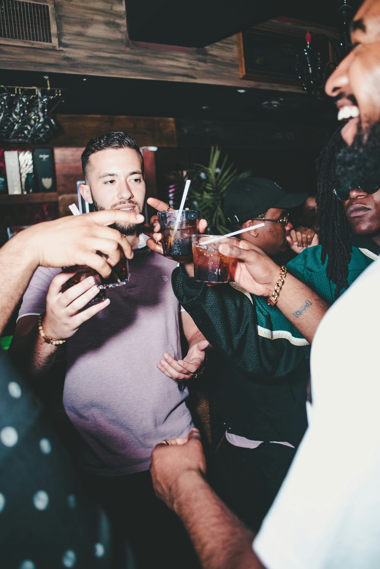Friends clinking cocktails and celebrating at a dimly lit nightclub party.