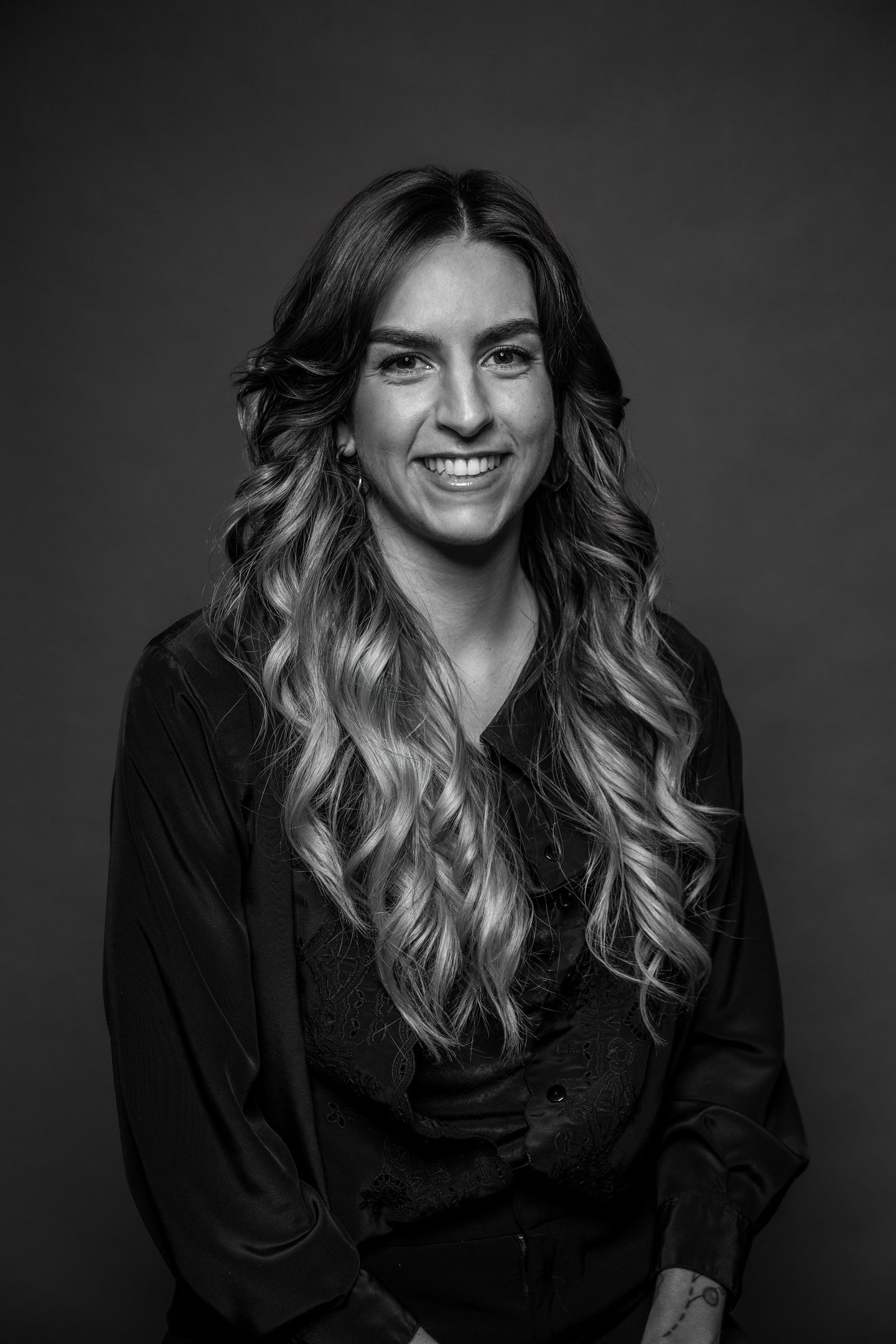 Portrait professionnel en noir et blanc d’une femme souriante aux longs cheveux ondulés portant un c