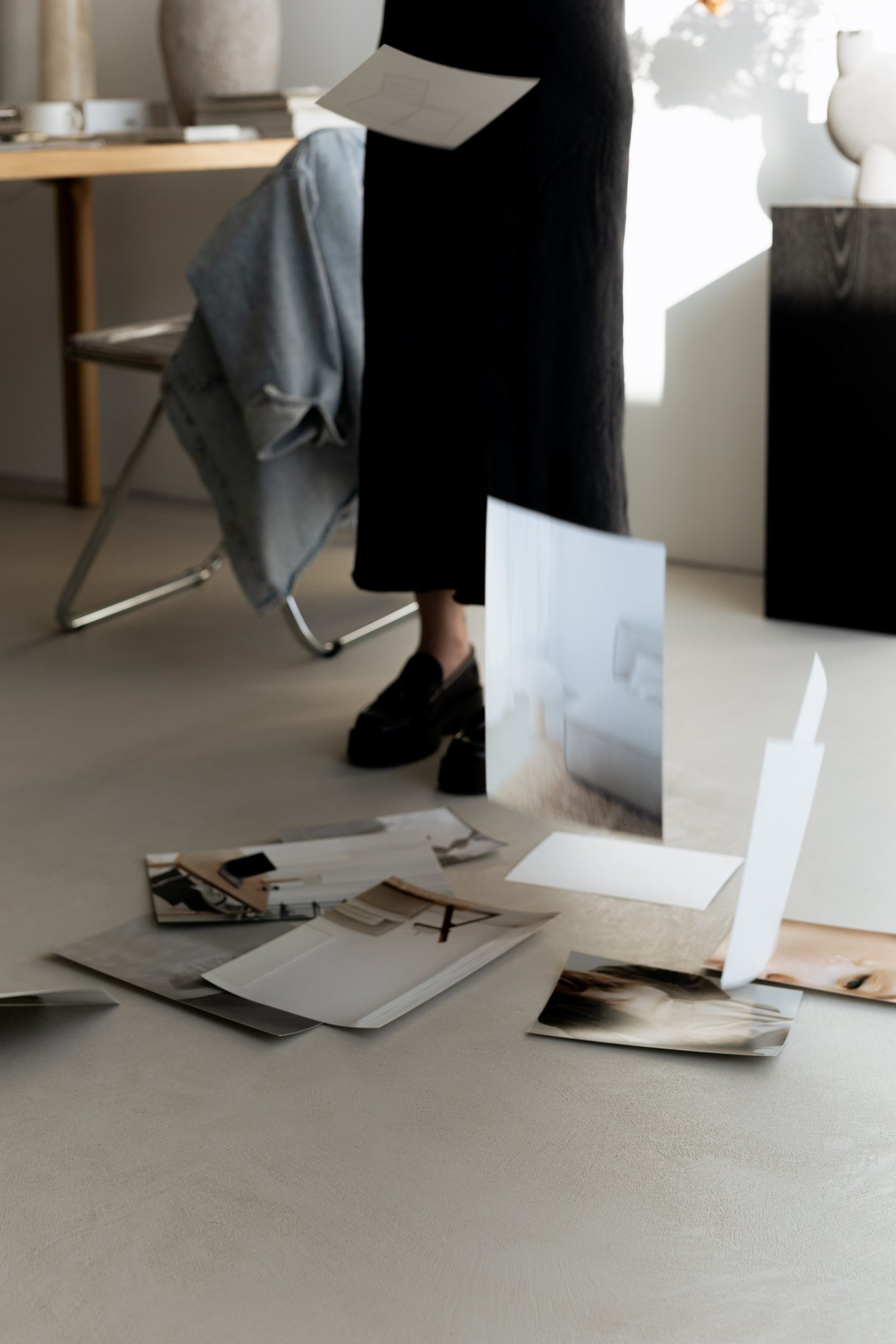 A woman in a minimalist studio dropping photography prints onto the floor for a mood board design.
