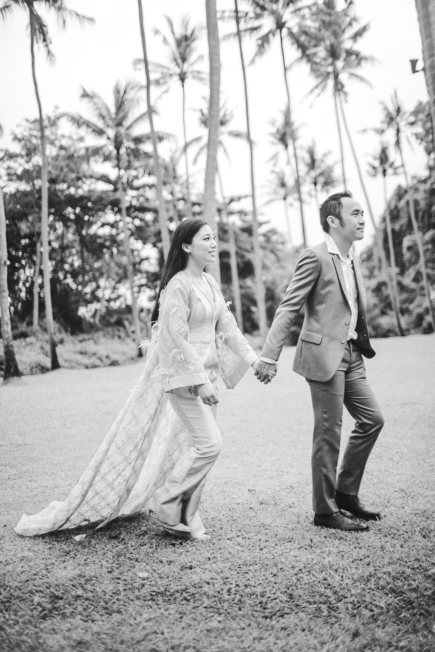 Black and white prewedding couple walking among palm trees at Amankila Karangasem