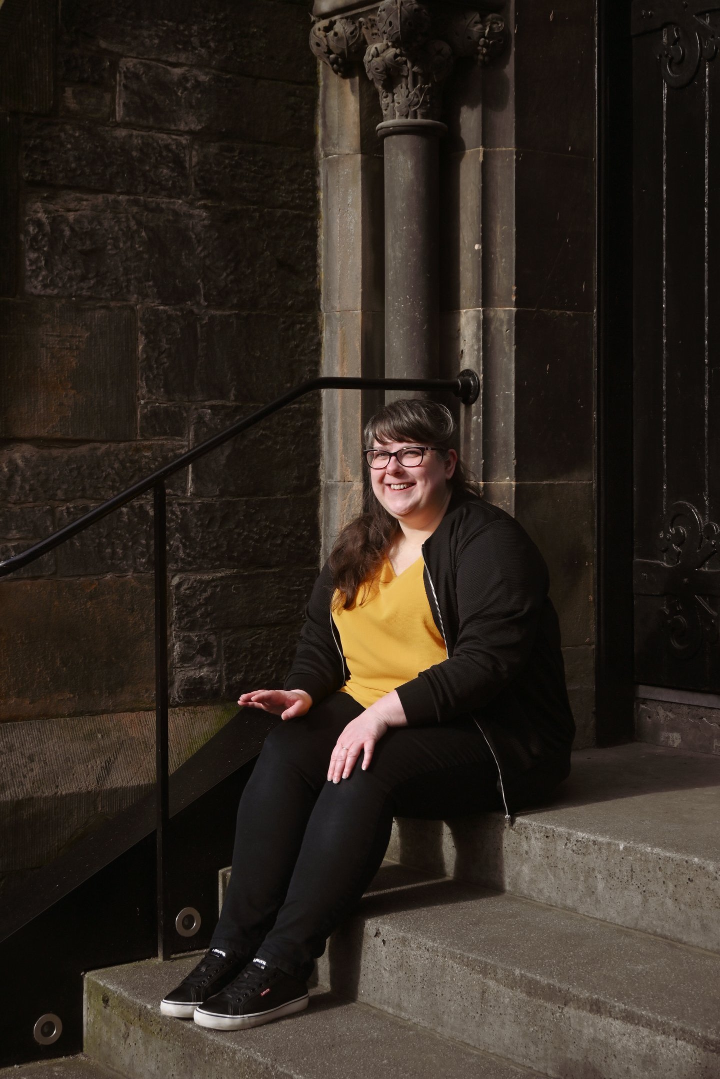 Laura is sitting on stone steps looking just off camera smiling at the sunshine