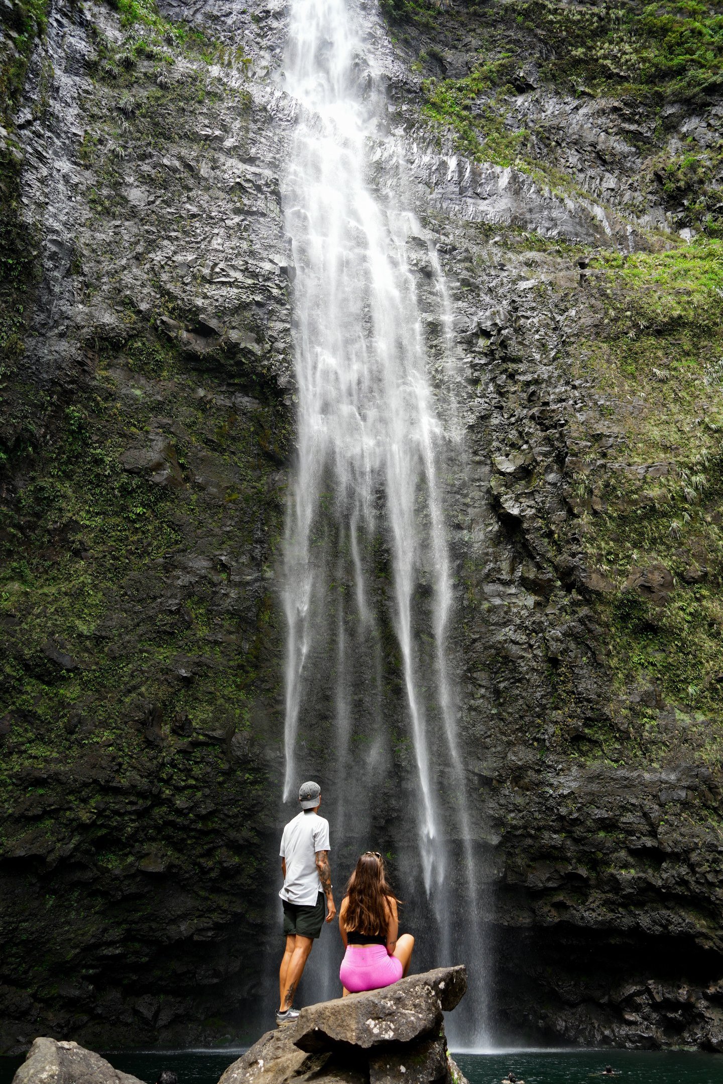 a couple of people standing in front of a waterfall in hawaii