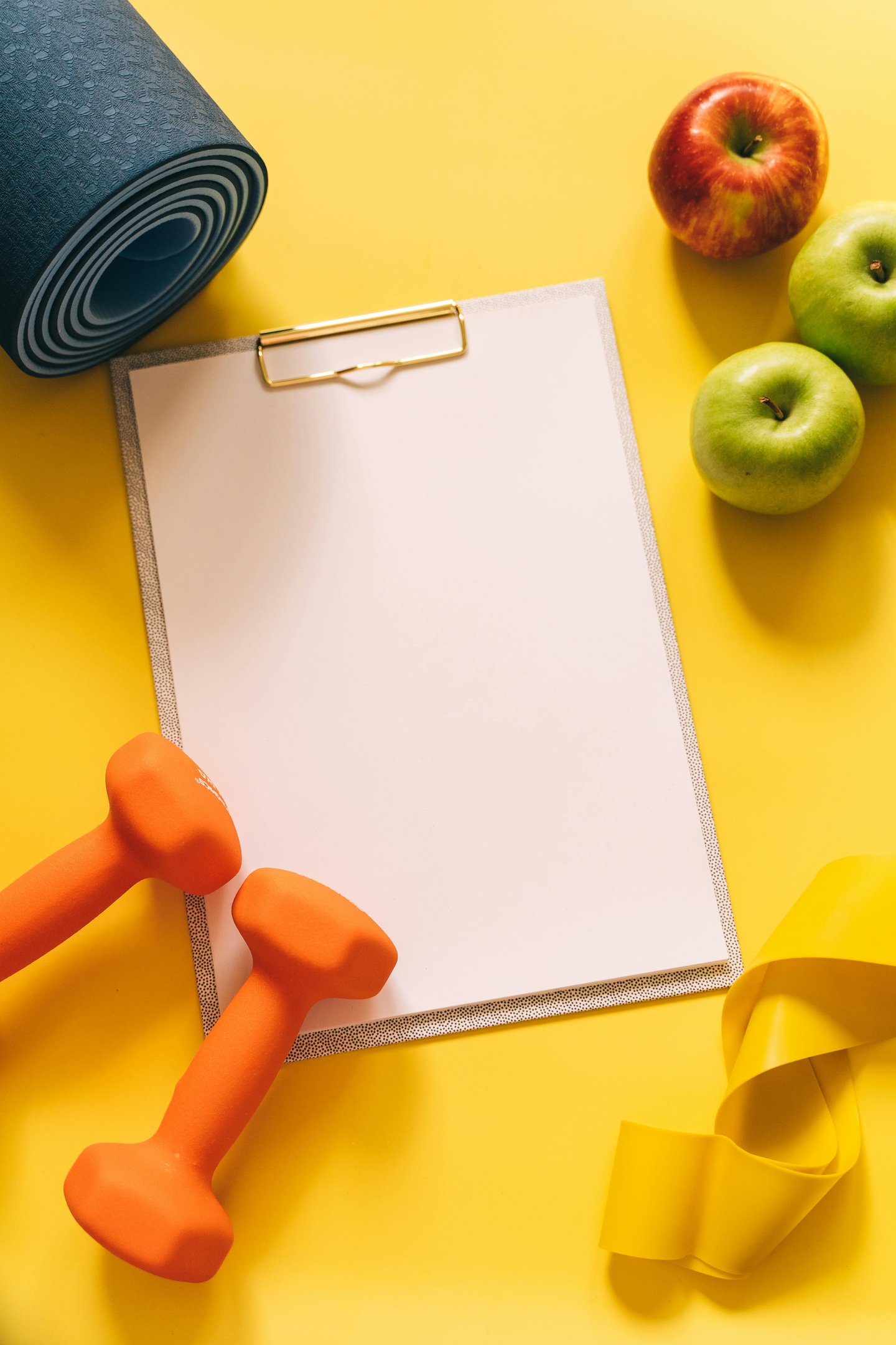 Bright flat‑lay wellness scene with a blue yoga mat, orange dumbbells, apples, a yellow resistance band,, yellow background