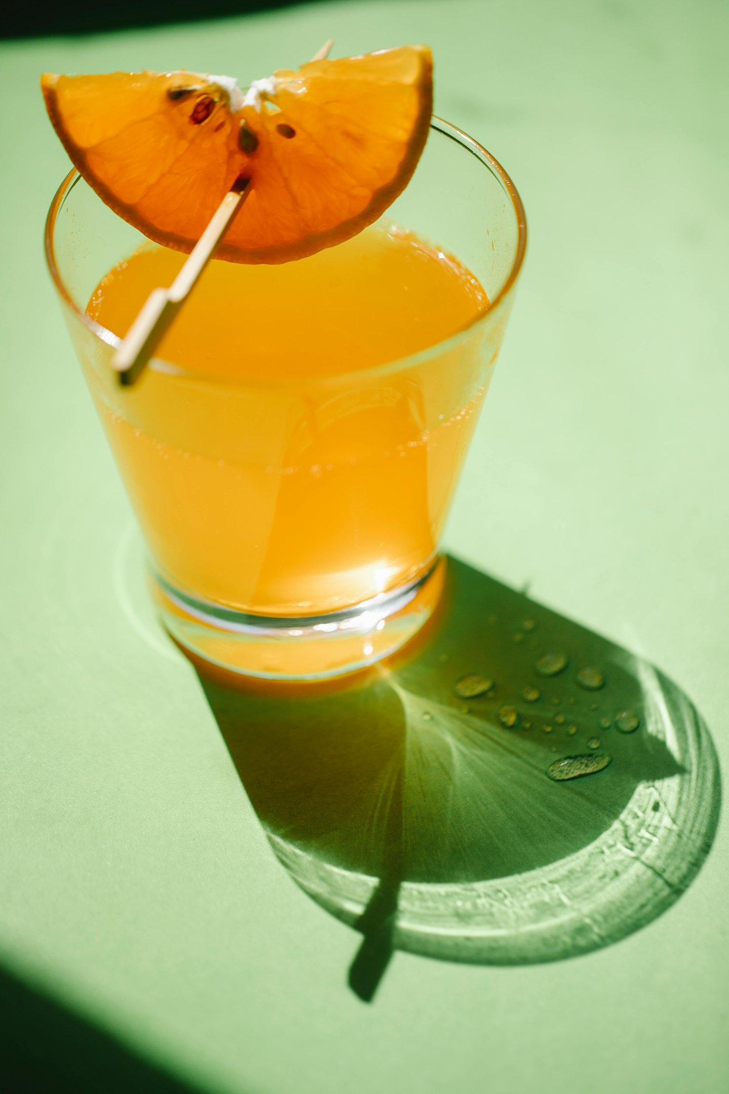 A clear glass filled with bright orange liquid on a light green surface