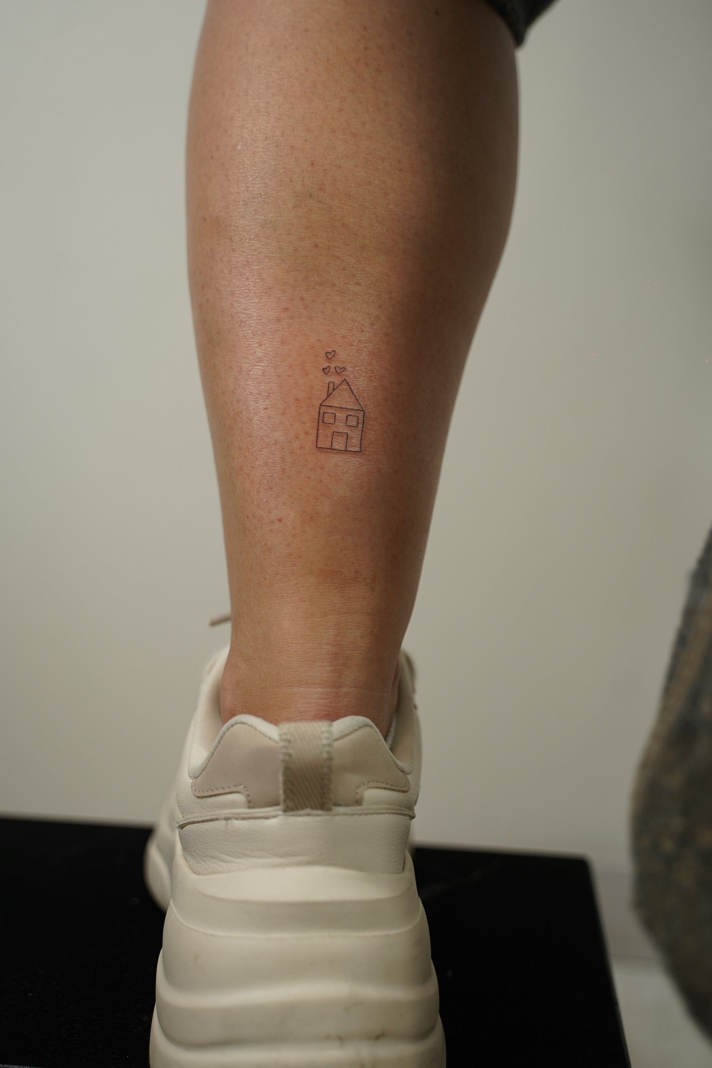 Tatuaje fineline en Madrid de casa pequeña con corazones flotando en trazo fino en el muslo
