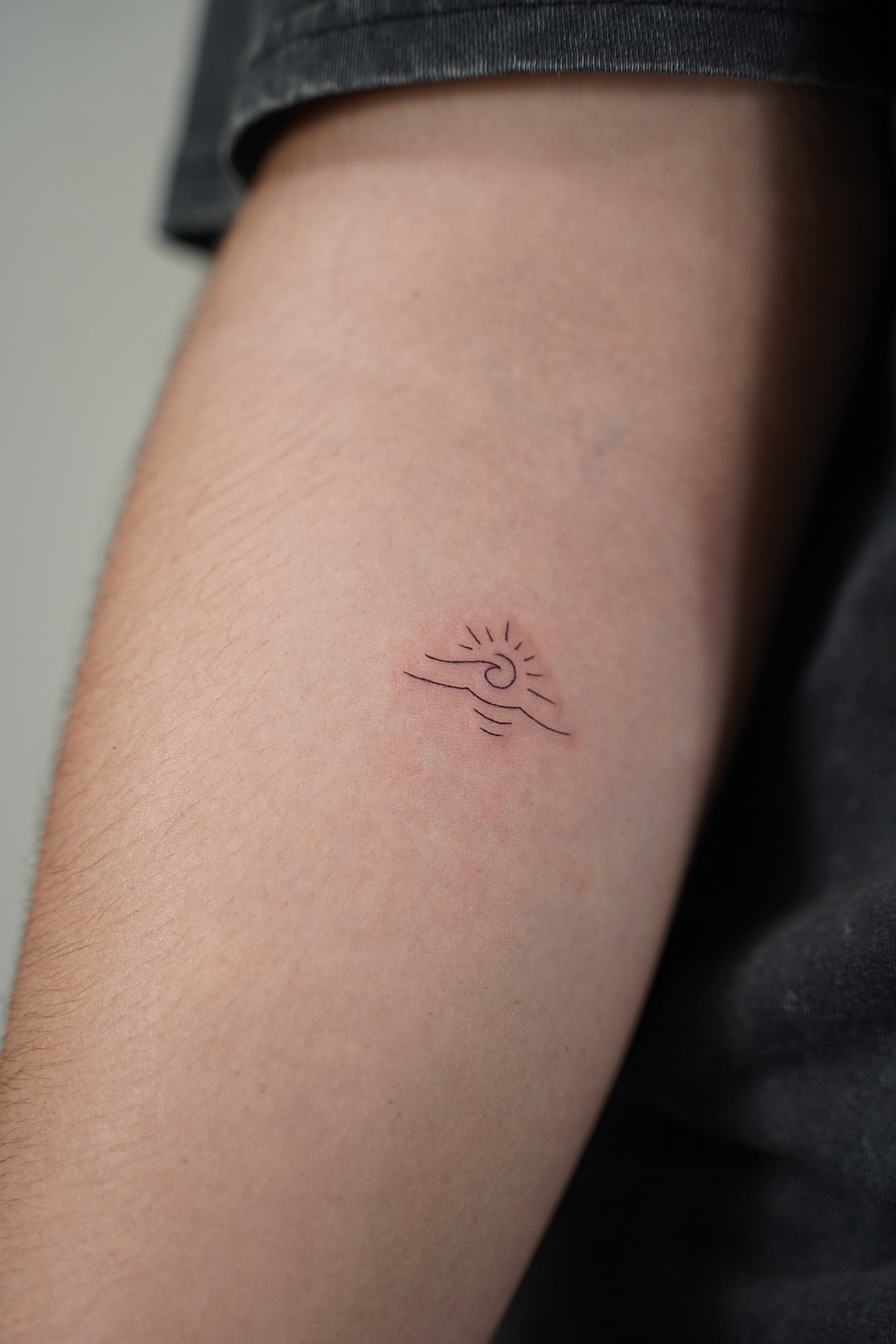 Tatuaje fineline en Madrid de sol con olas minimalista en trazo fino en el antebrazo