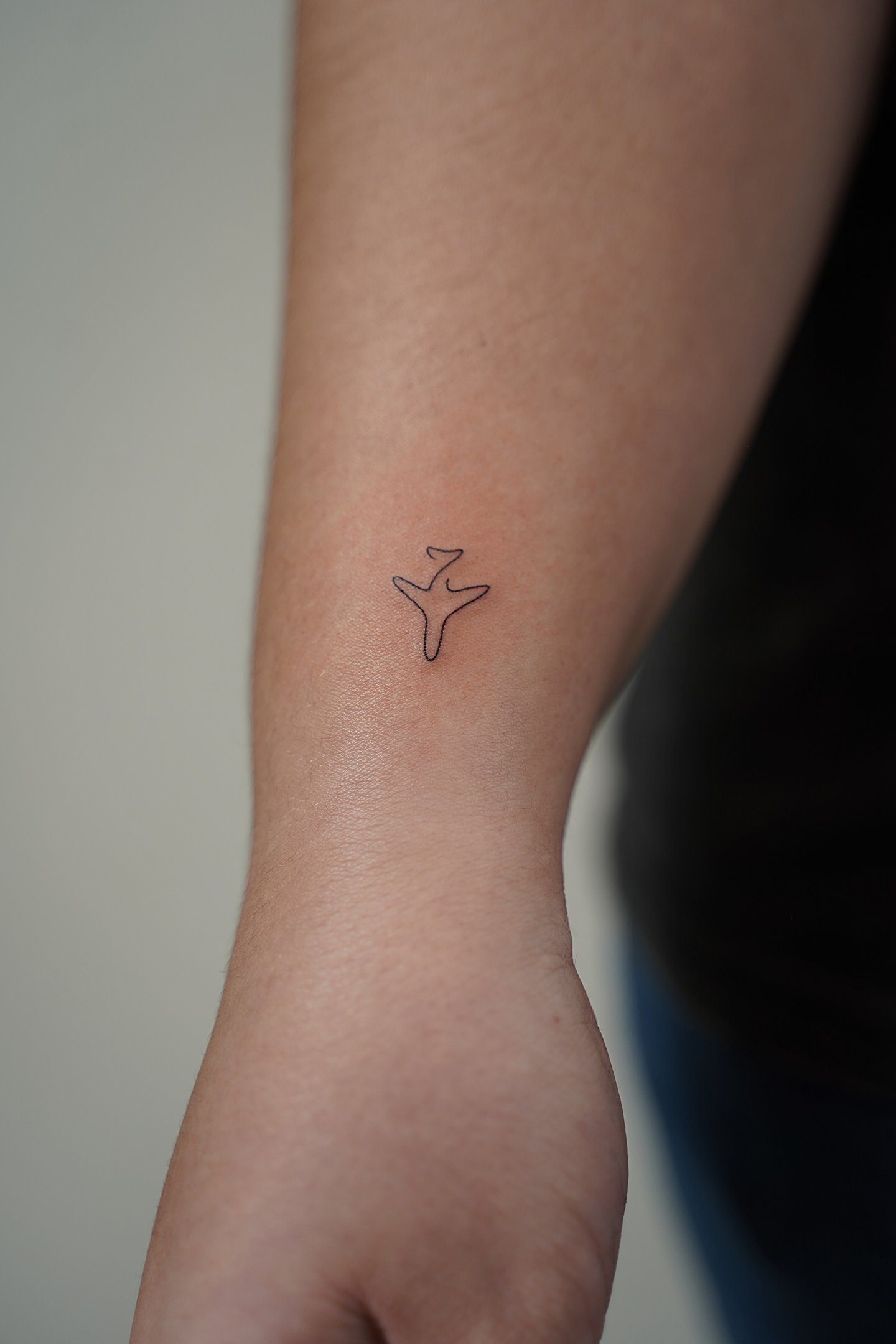 Tatuaje fineline en Madrid de avión pequeño en trazo continuo y minimalista en el antebrazo