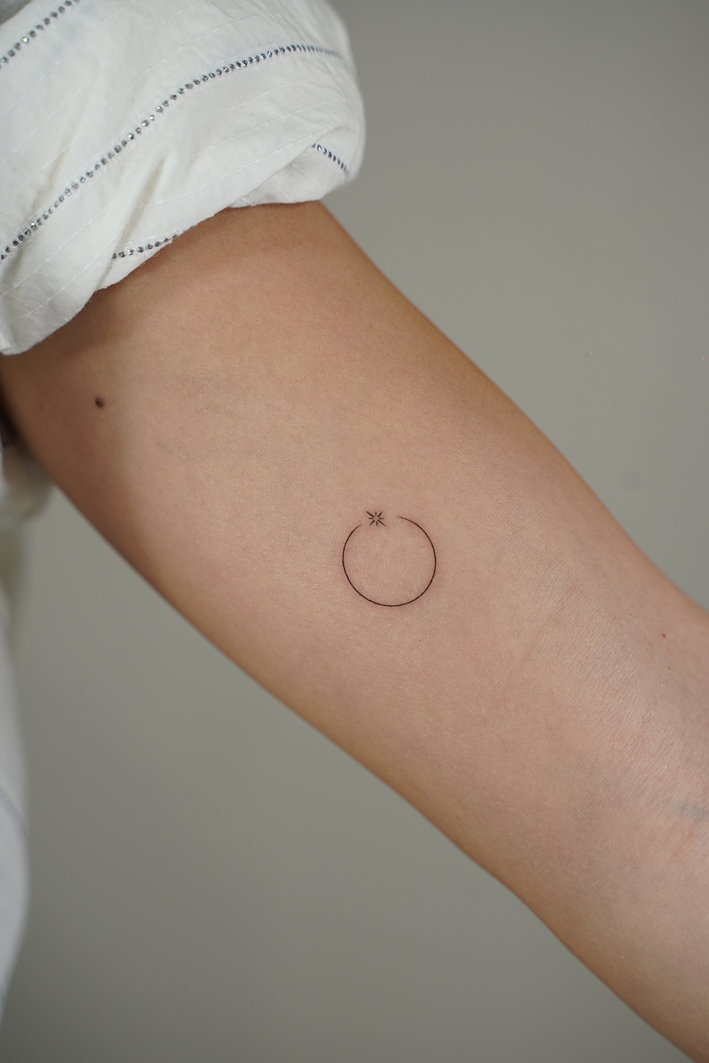 Tatuaje fineline en Madrid de círculo minimalista con estrella pequeña en trazo fino en el antebrazo