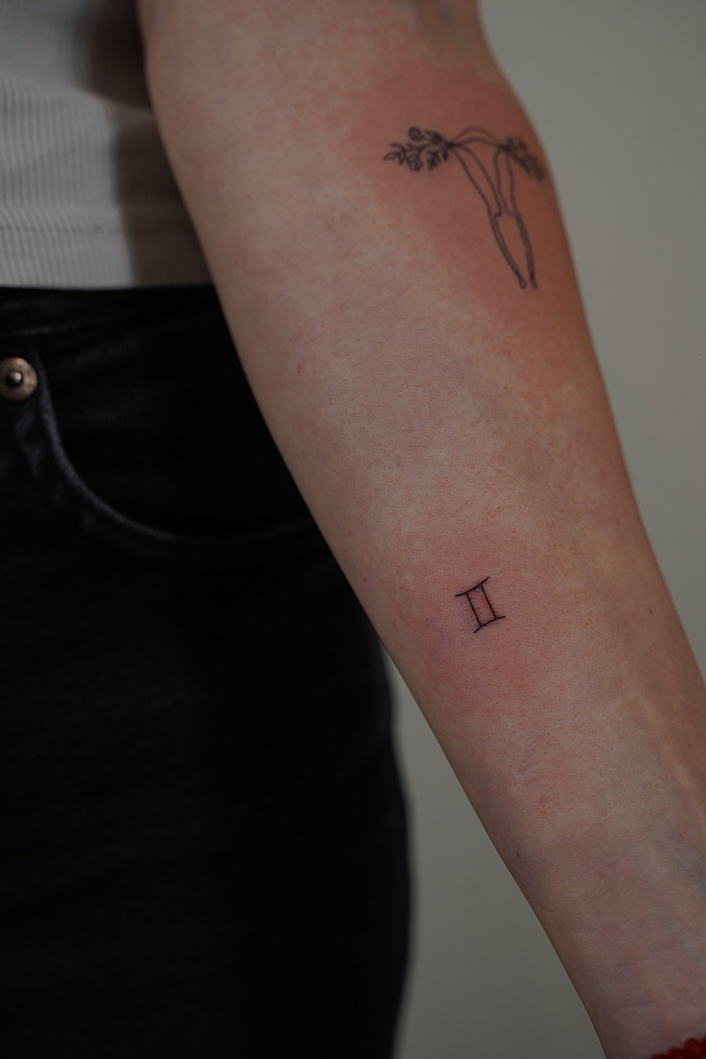 Tatuaje fineline en Madrid de símbolo del zodiaco Géminis en trazo fino en el antebrazo