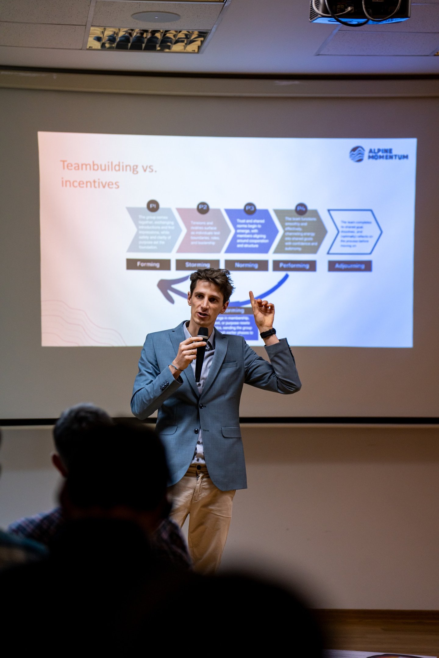 A male speaker presenting Tuckman's stages of team development at a corporate teambuilding workshop.