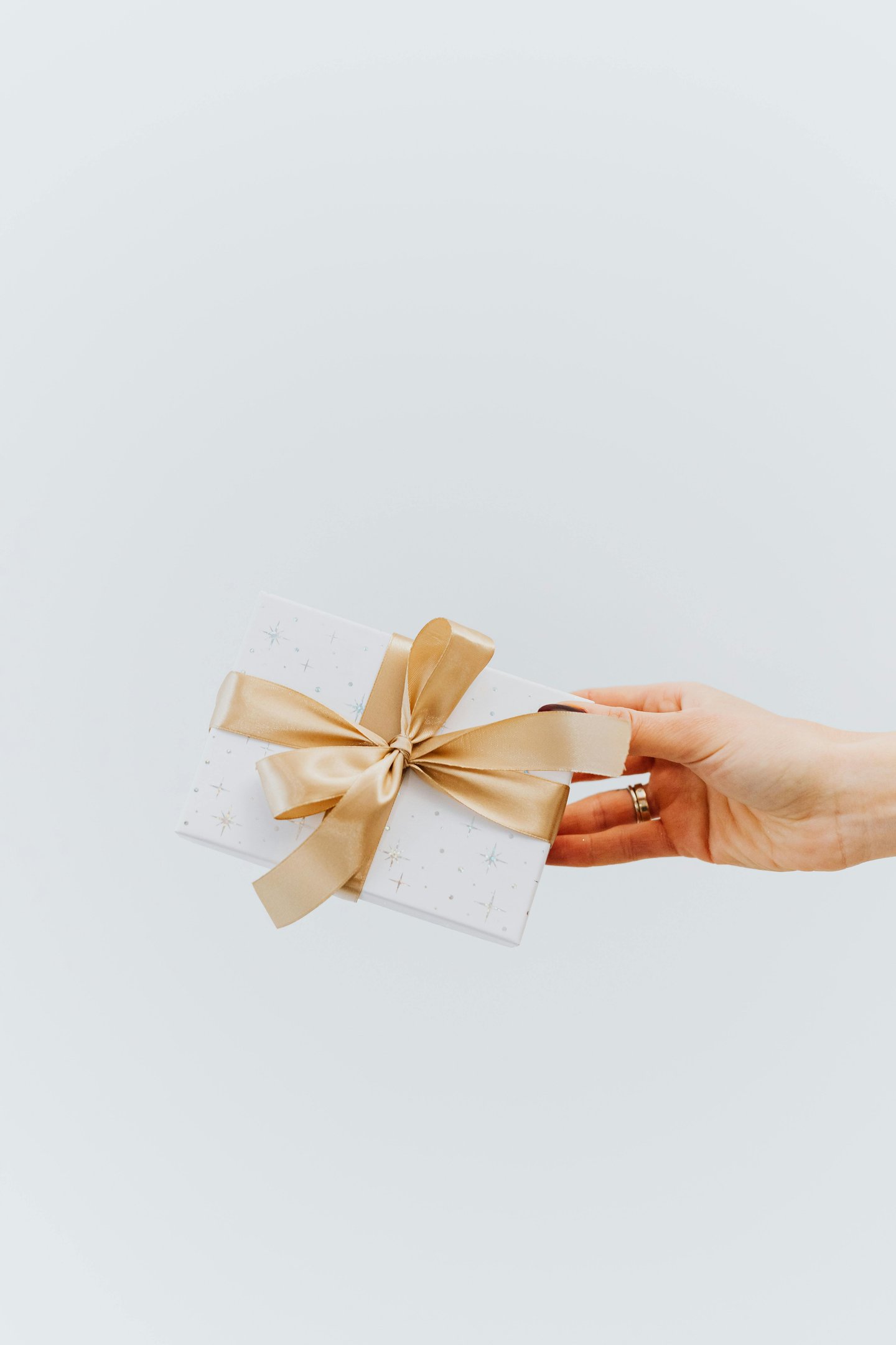 Woman's hand holding a gift card wrapped in white paper and with a gold bow