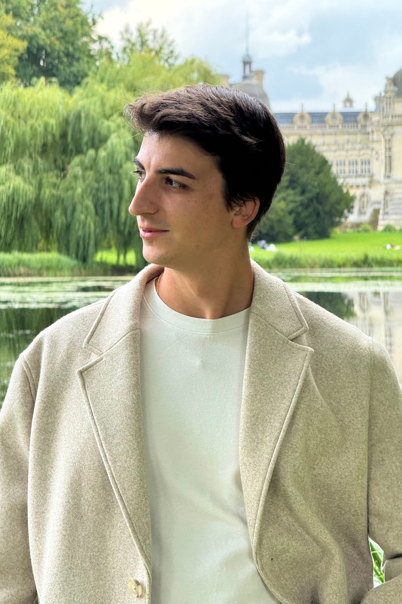 Créateur de DigiMagnat, en manteau de laine beige, posant devant un château historique