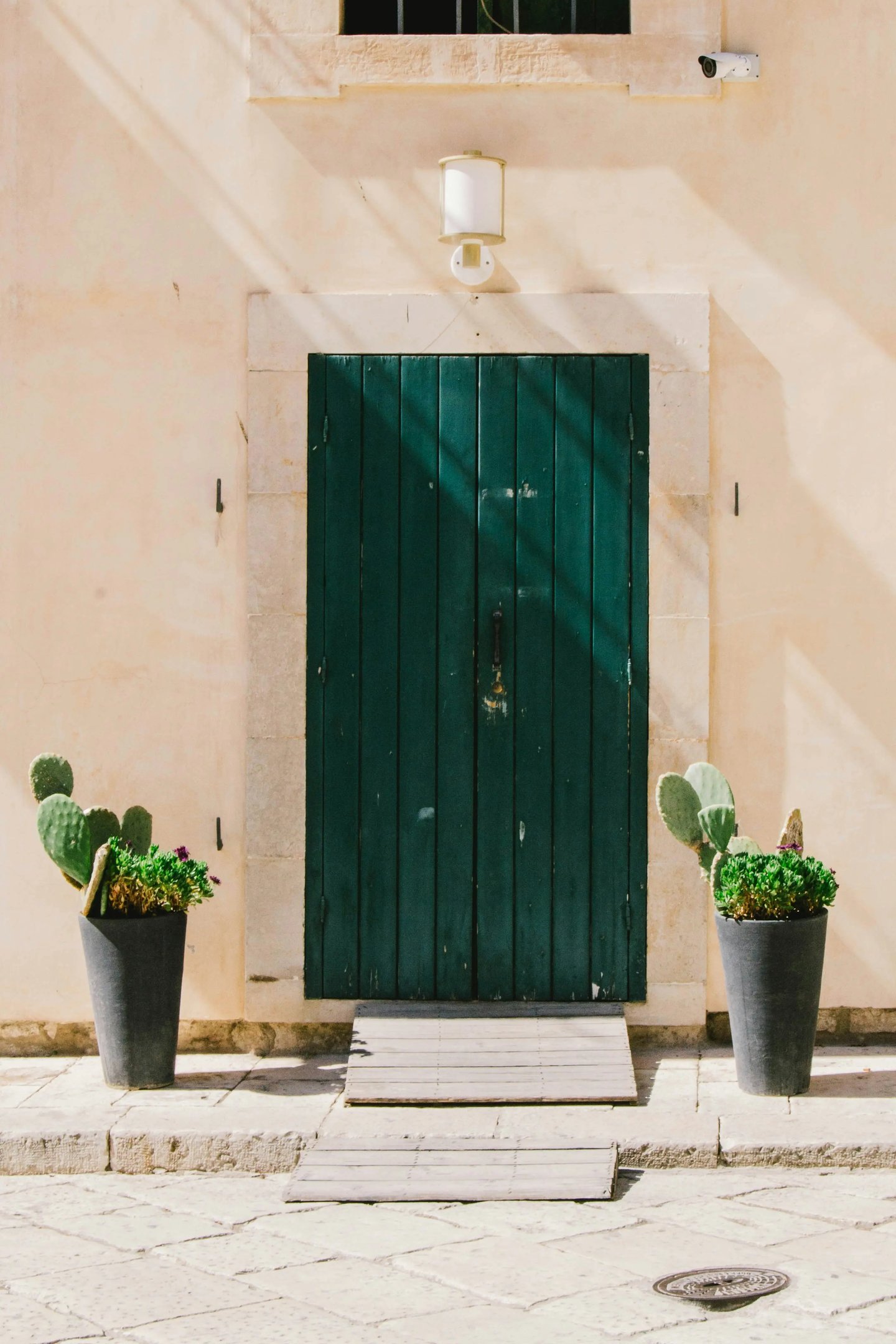 itahome luxury Rustic dark green wooden door on a beige stone wall flanked by potted cactus plants.