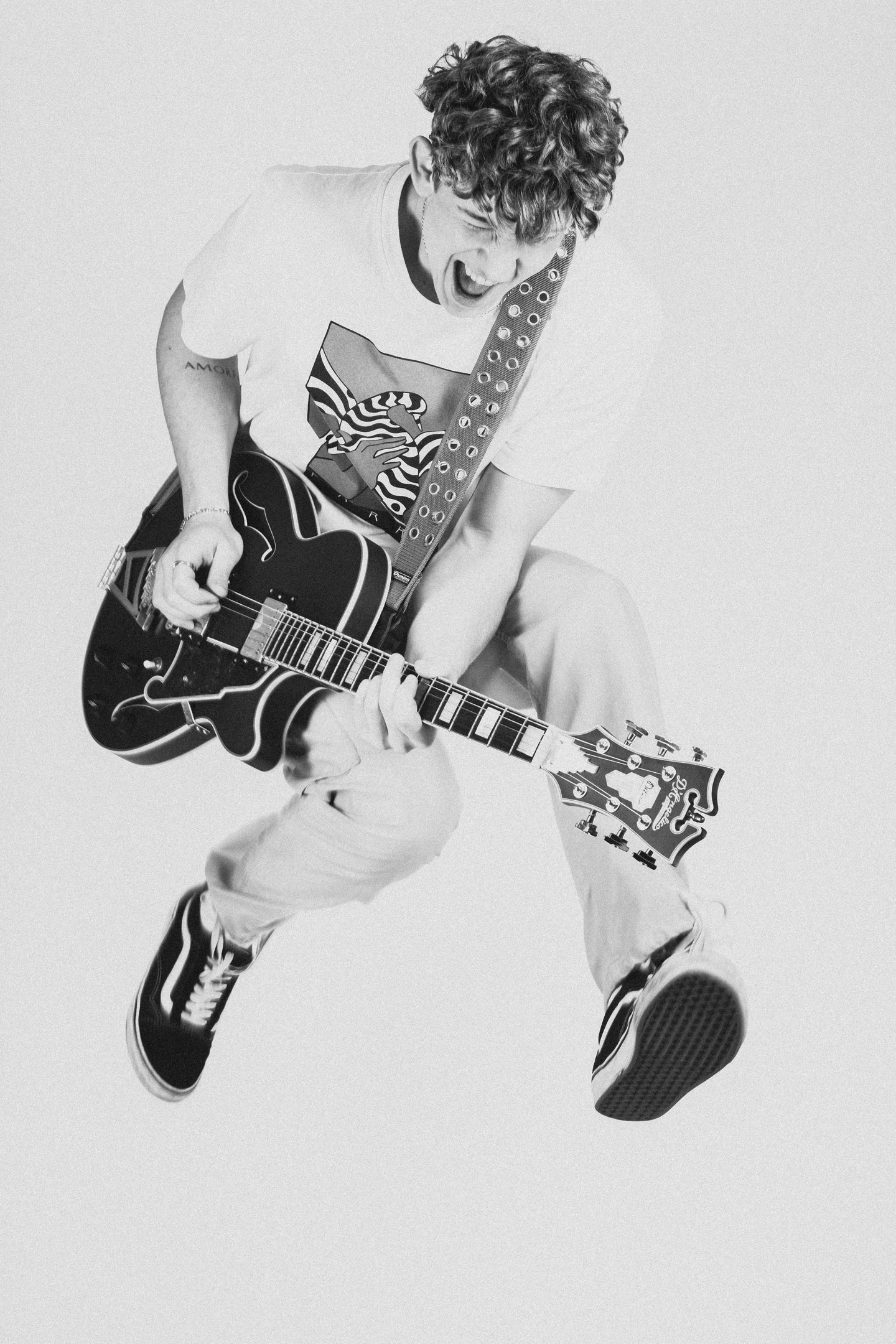 portrait of a man jumping in a white shirt and tie dye on a guitar