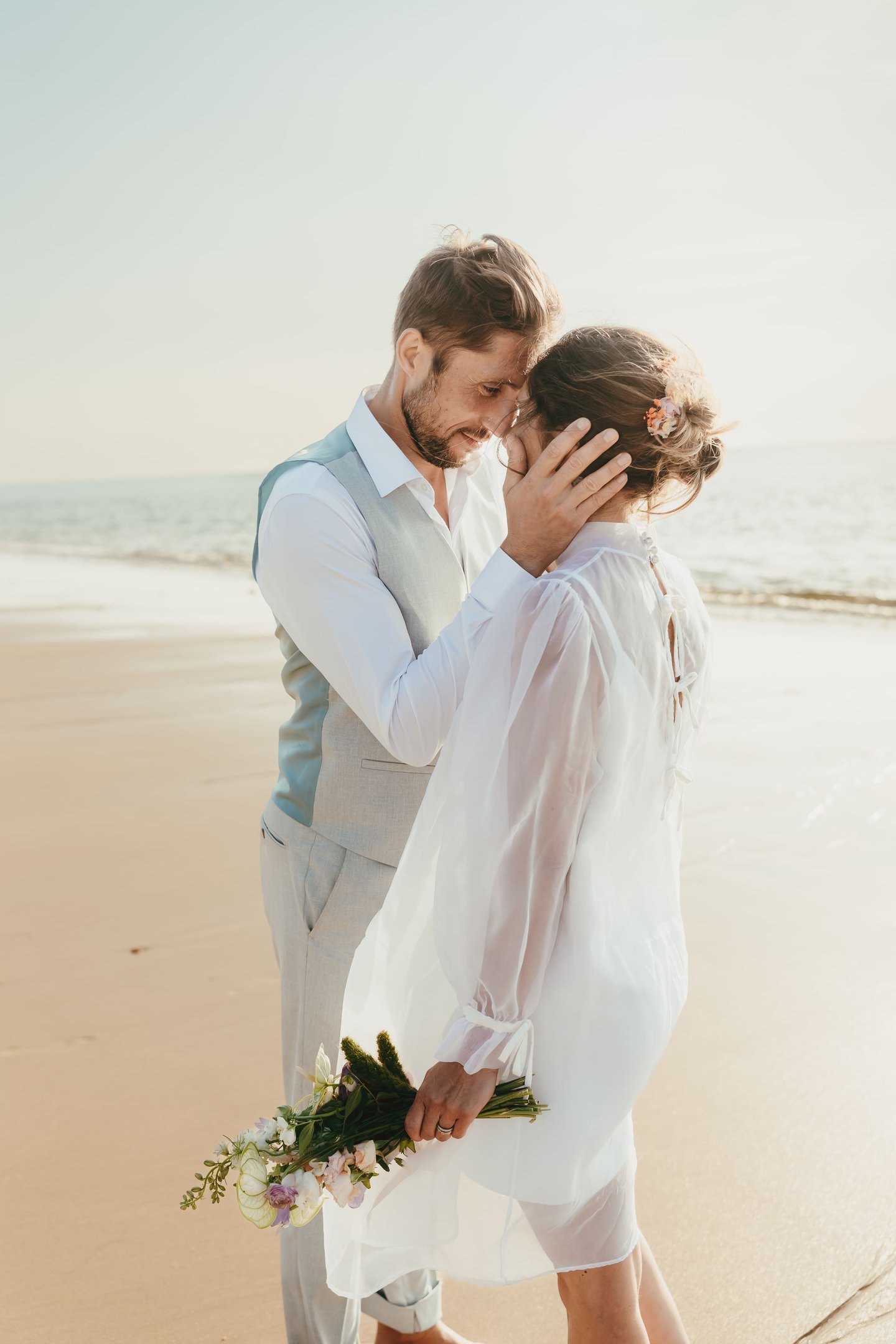 A romantic bride and groom embrace during a sunny destination beach wedding ceremony.