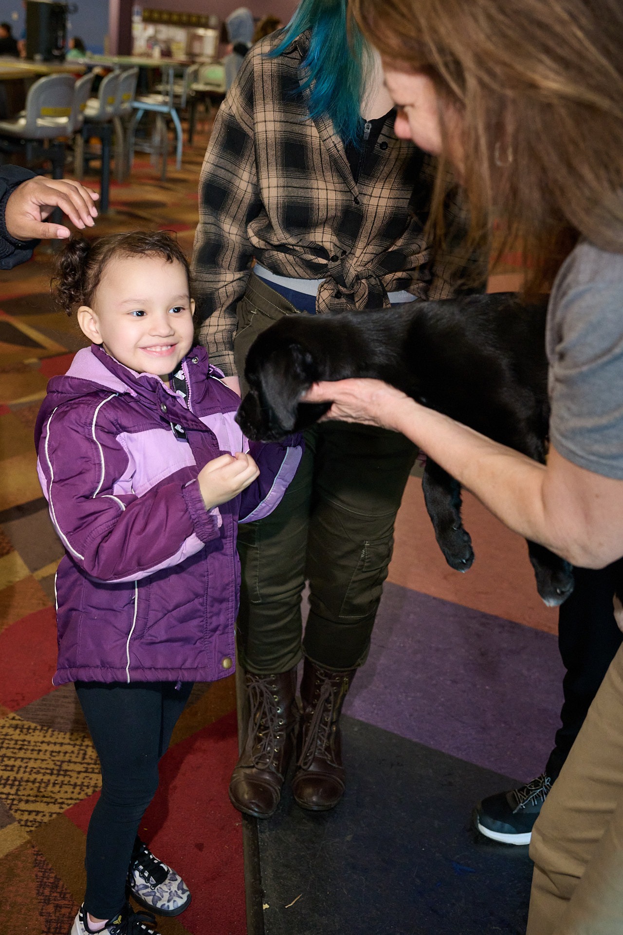 a woman holding a black puppy to a girl in a purple jacket 