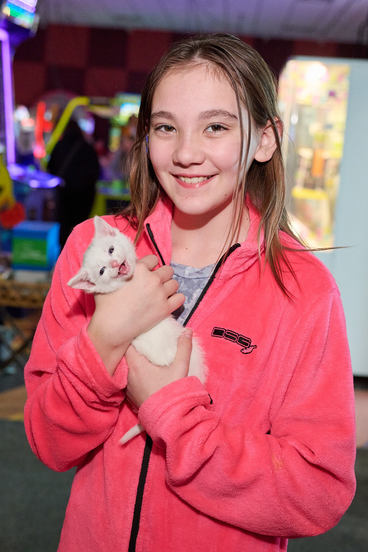 a girl in a pink jacket holding a white kitten