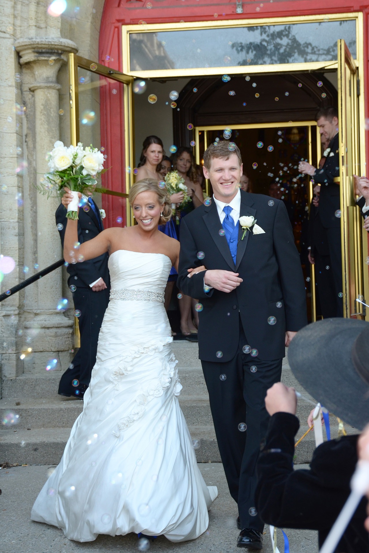 a bride and groom walking down the aisle of a wedding from church with bubbles generated by guests