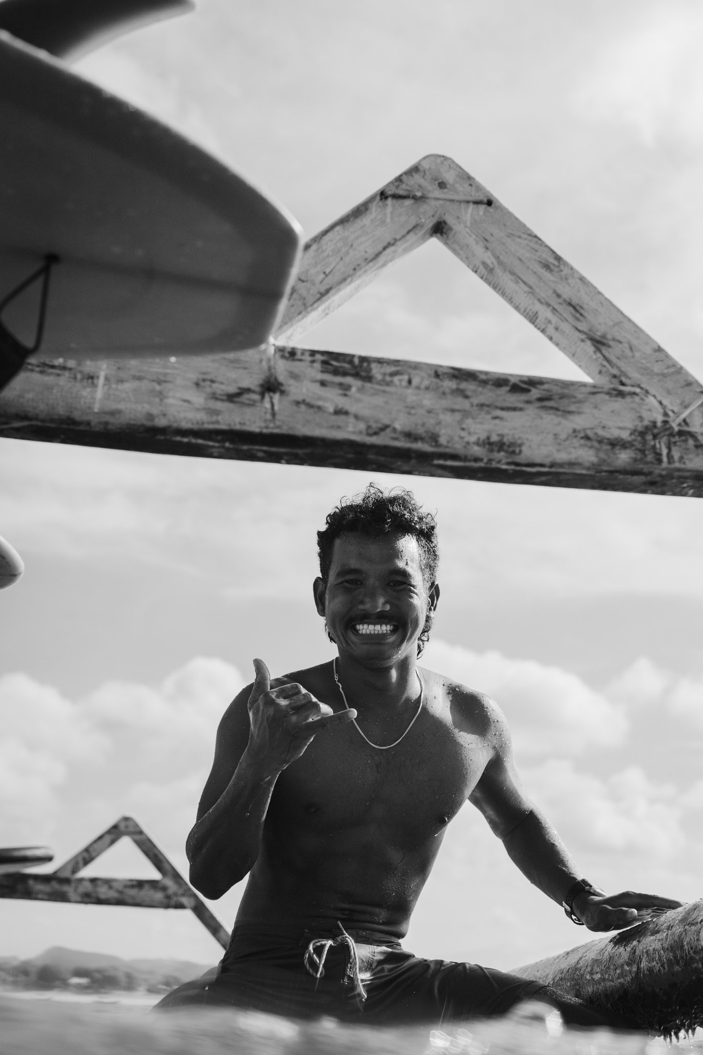 Black and white photo of the surf school owner on his surfboard showing a shaka gesture.