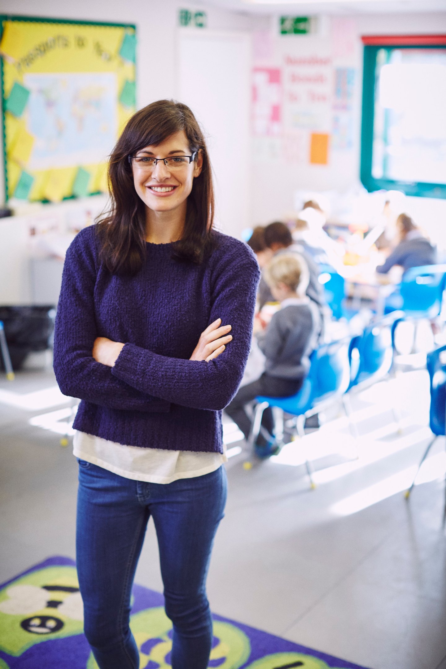 a woman in a purple sweater and jeans standing in a classroom