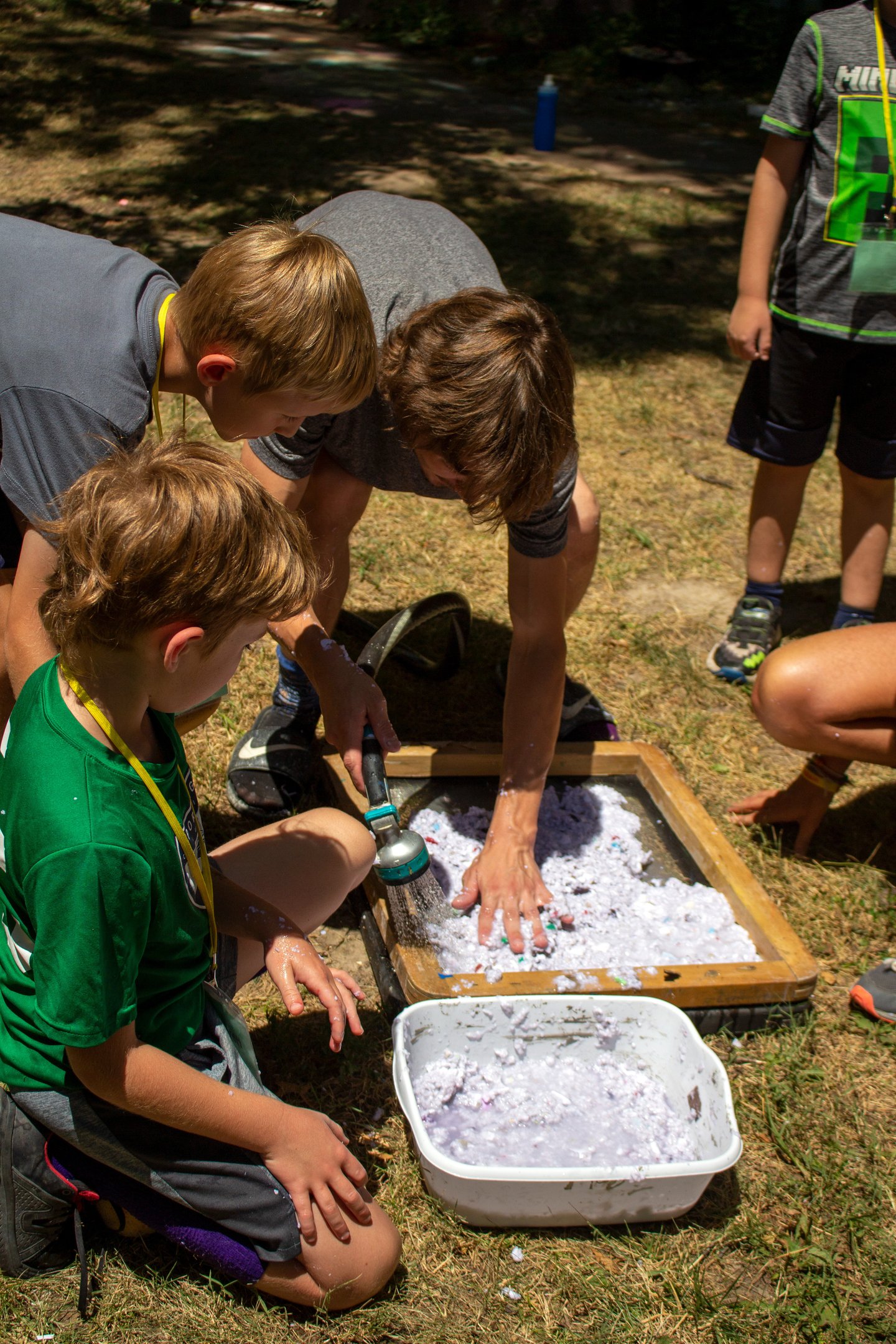 Teacher using a hose to spray shredded paper onto a screen with kids surrounding.