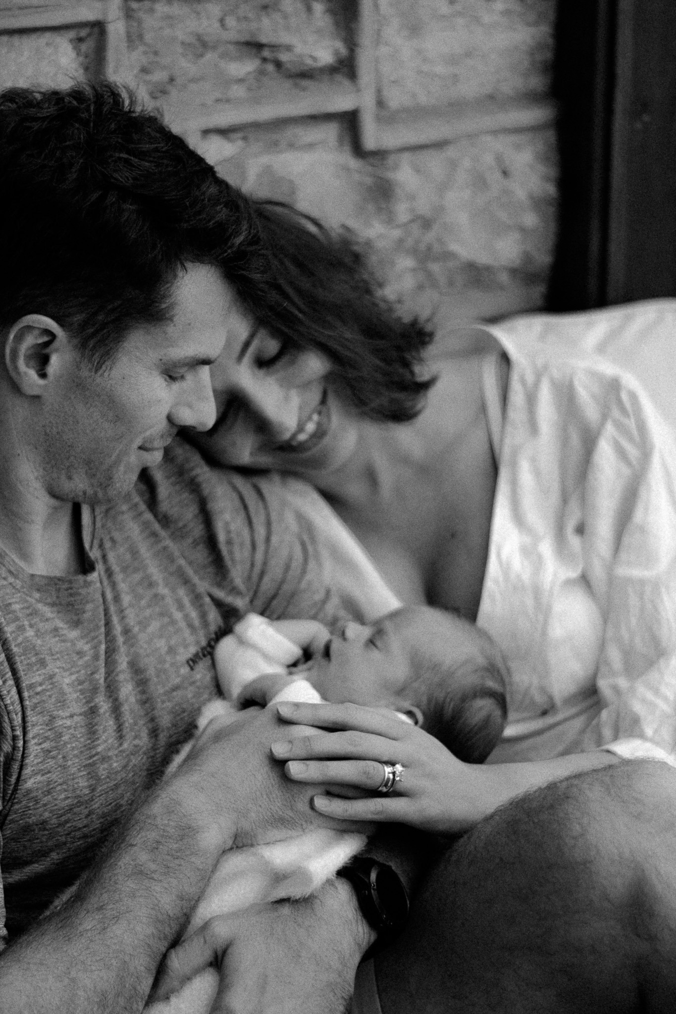 a newborn in her mom & dads arms, looking down at her in a lifestyle newborn shoot