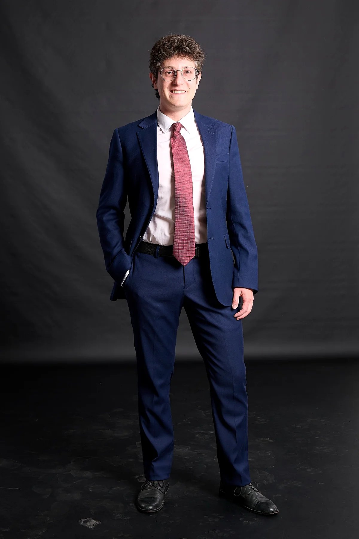 Professional man in a blue tailored suit and red tie posing for a corporate headshot.