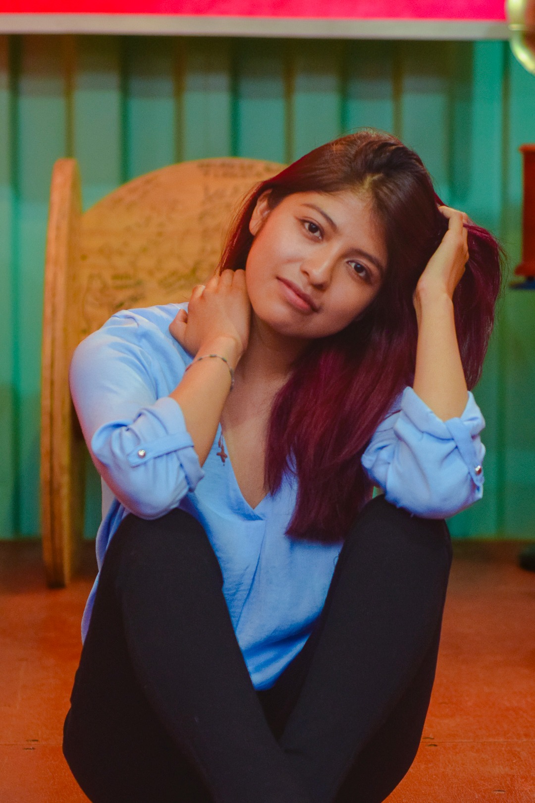 Young woman with auburn hair in a blue shirt sitting on the floor in a studio setting.