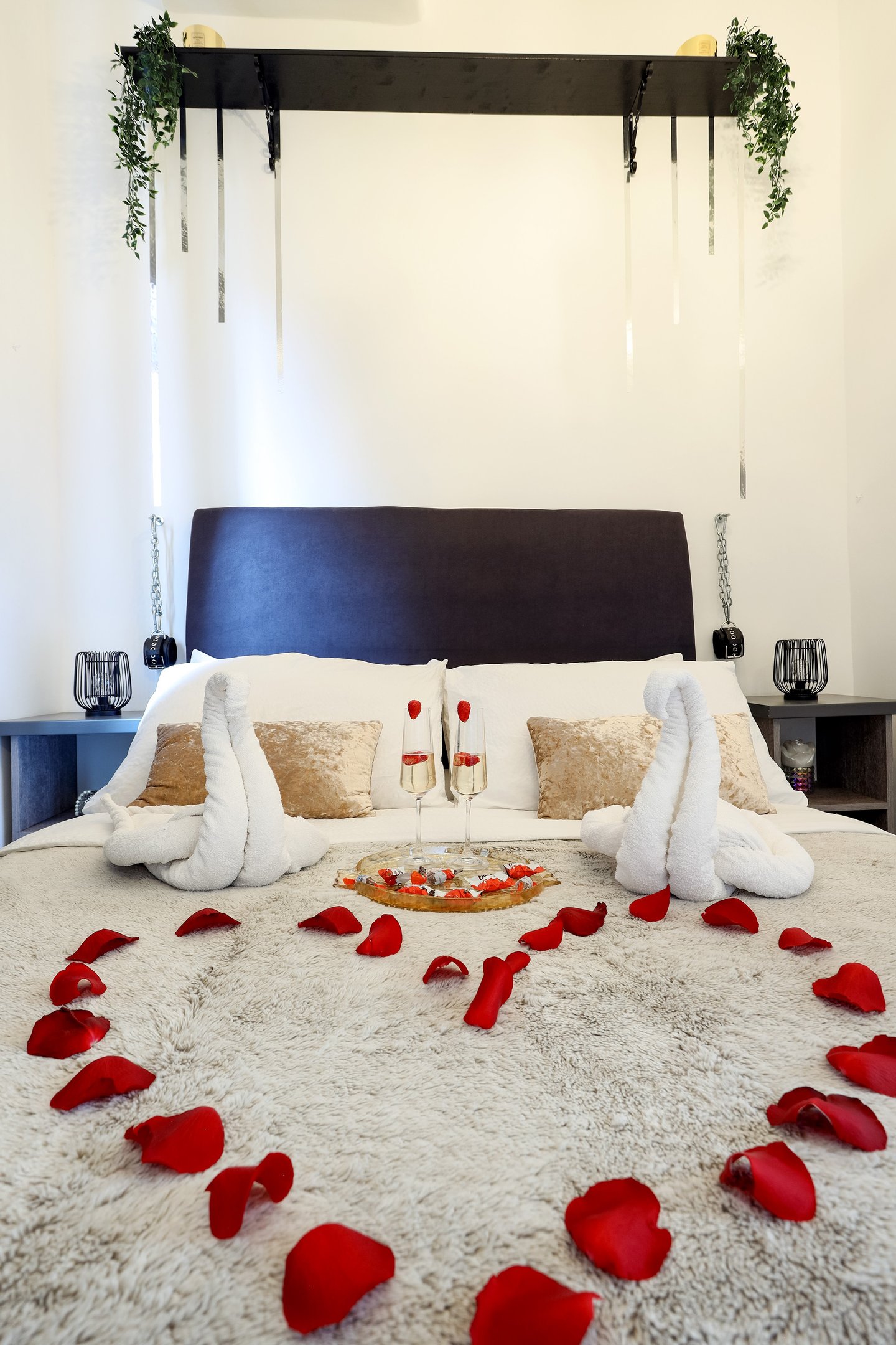The photo shows a bed decorated for a honeymoon special in the BDSM Love Apartment with champagne and rose petals.