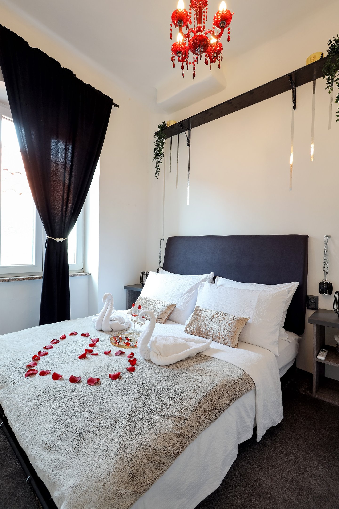 The photo shows honeymoon special setting of the bedroom in the BDSM Love Apartment. Champagne, rose petals, restraints.