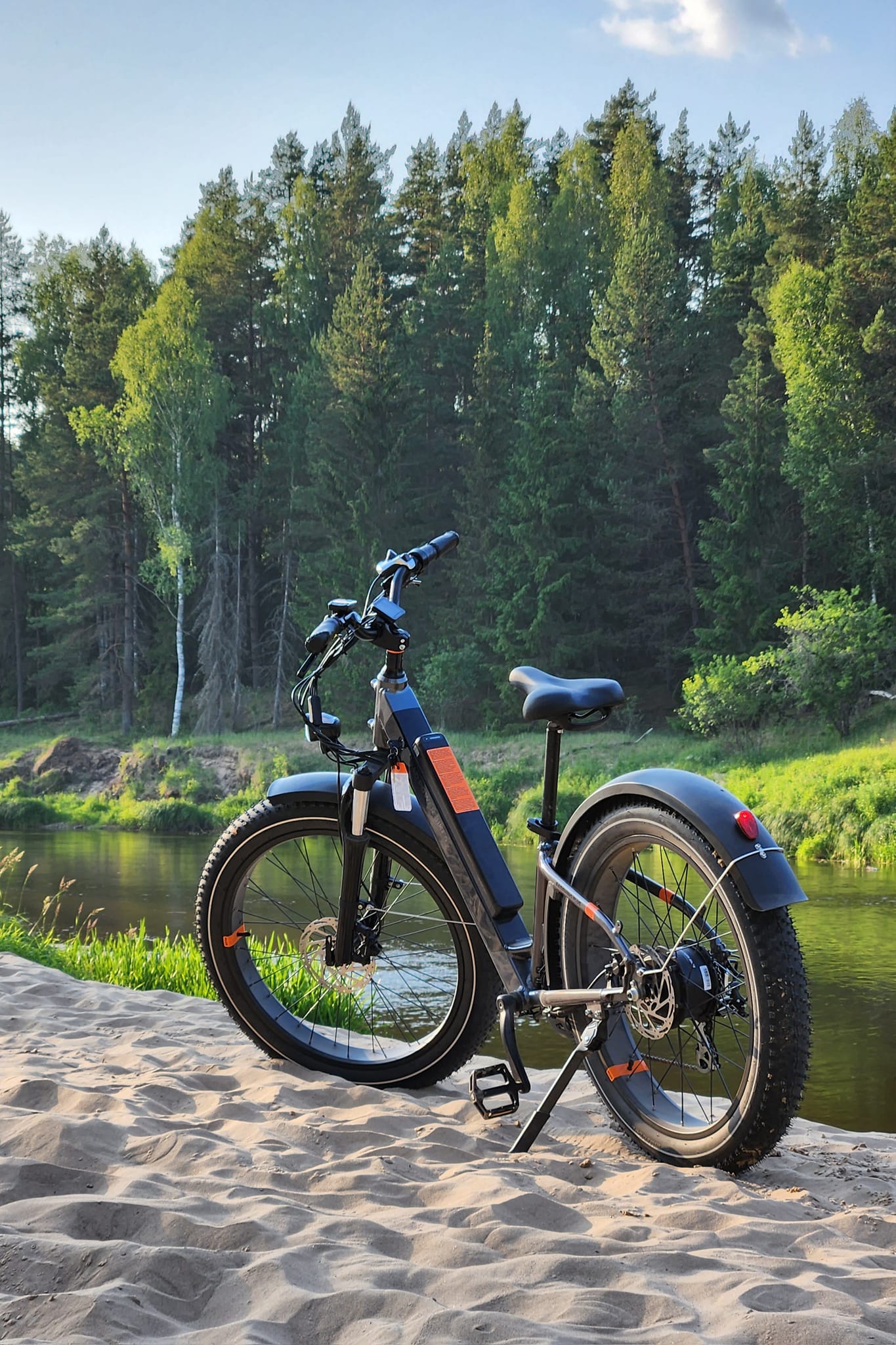 a fat tire electric rental bicycle parked on sand near a river
