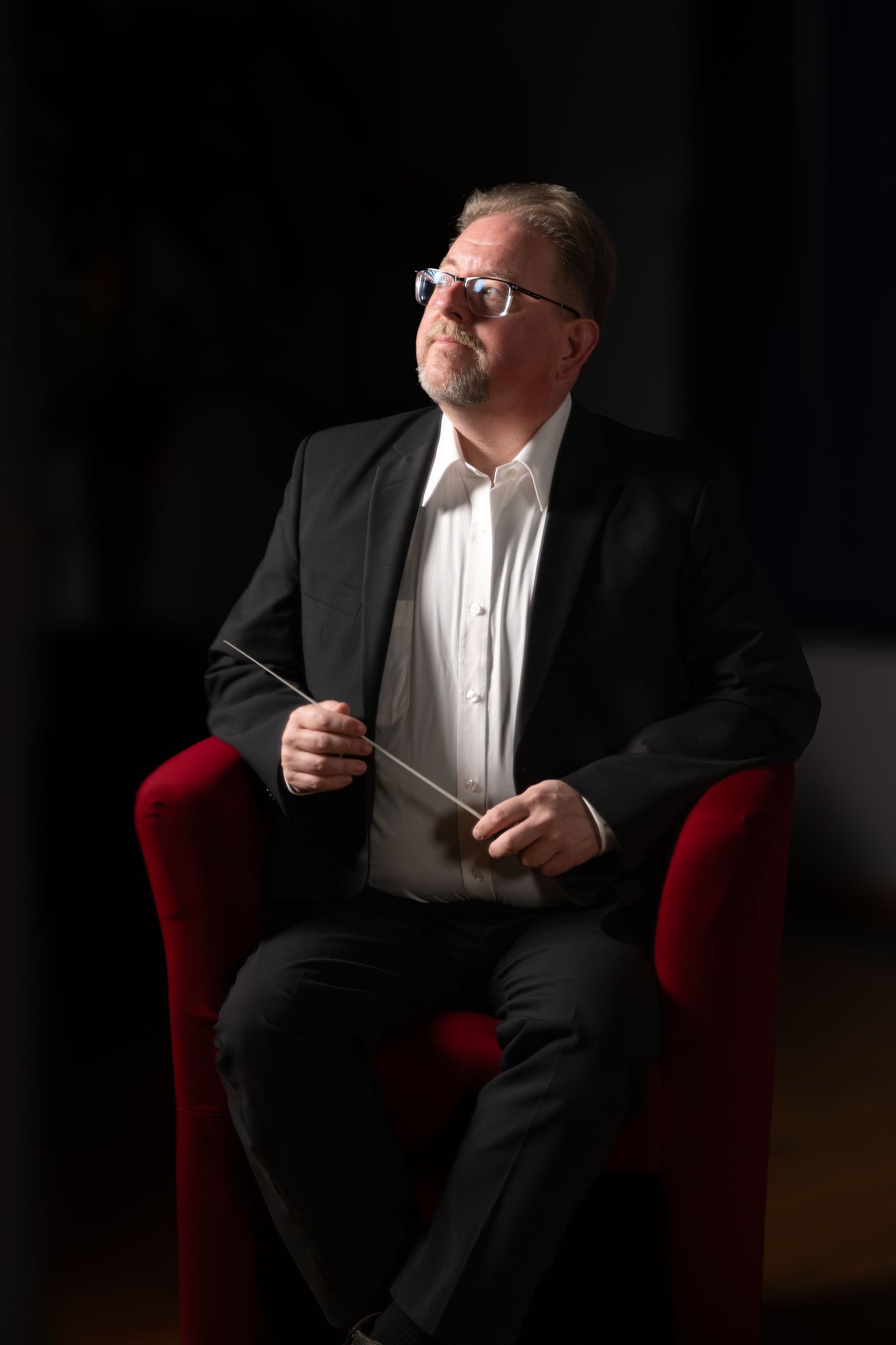 Robert in a suit and tie is holding a conductor's baton