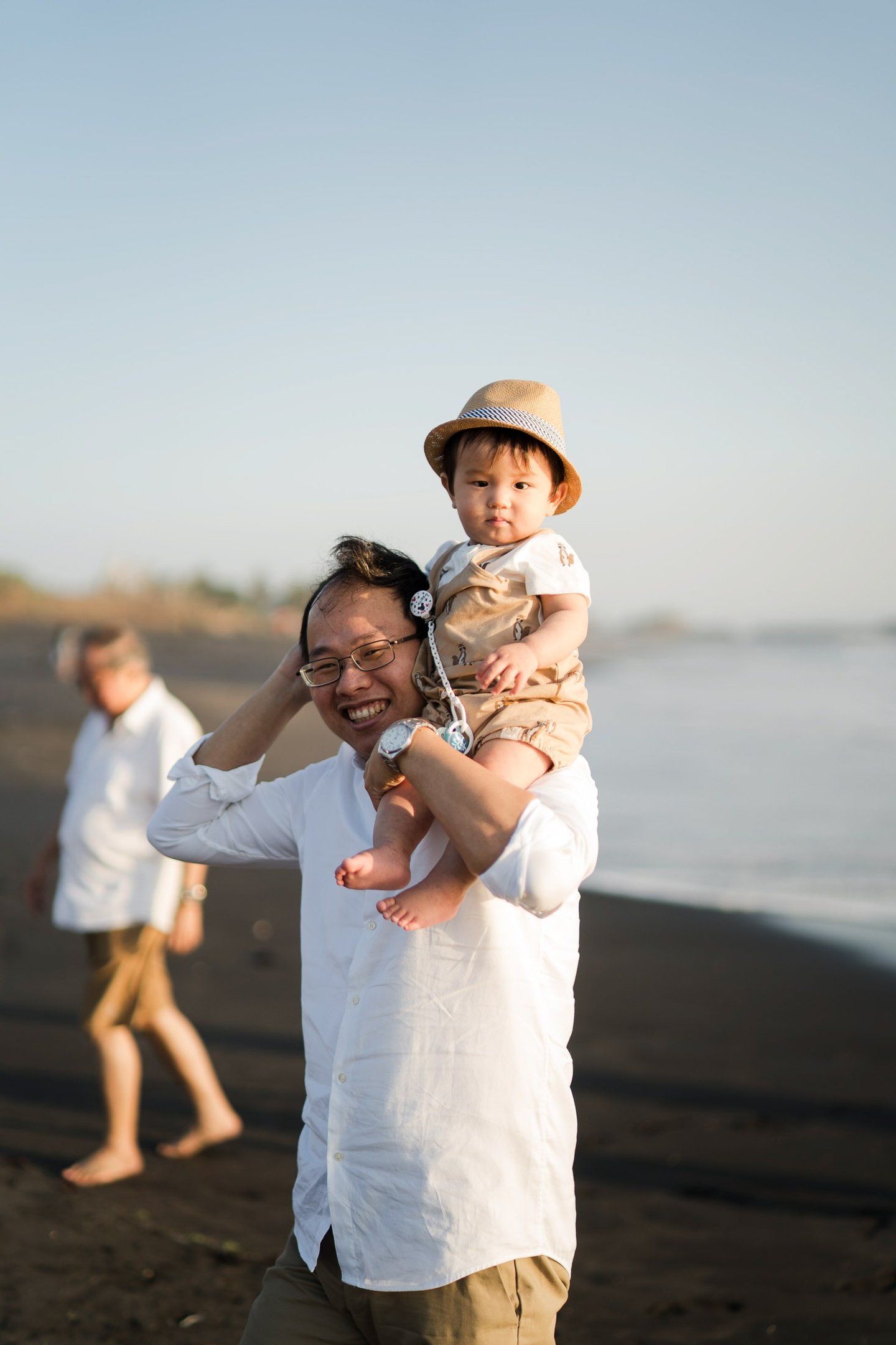 Father carrying his child on the black sand beach during a family photography session at Nyanyi Beach Bali