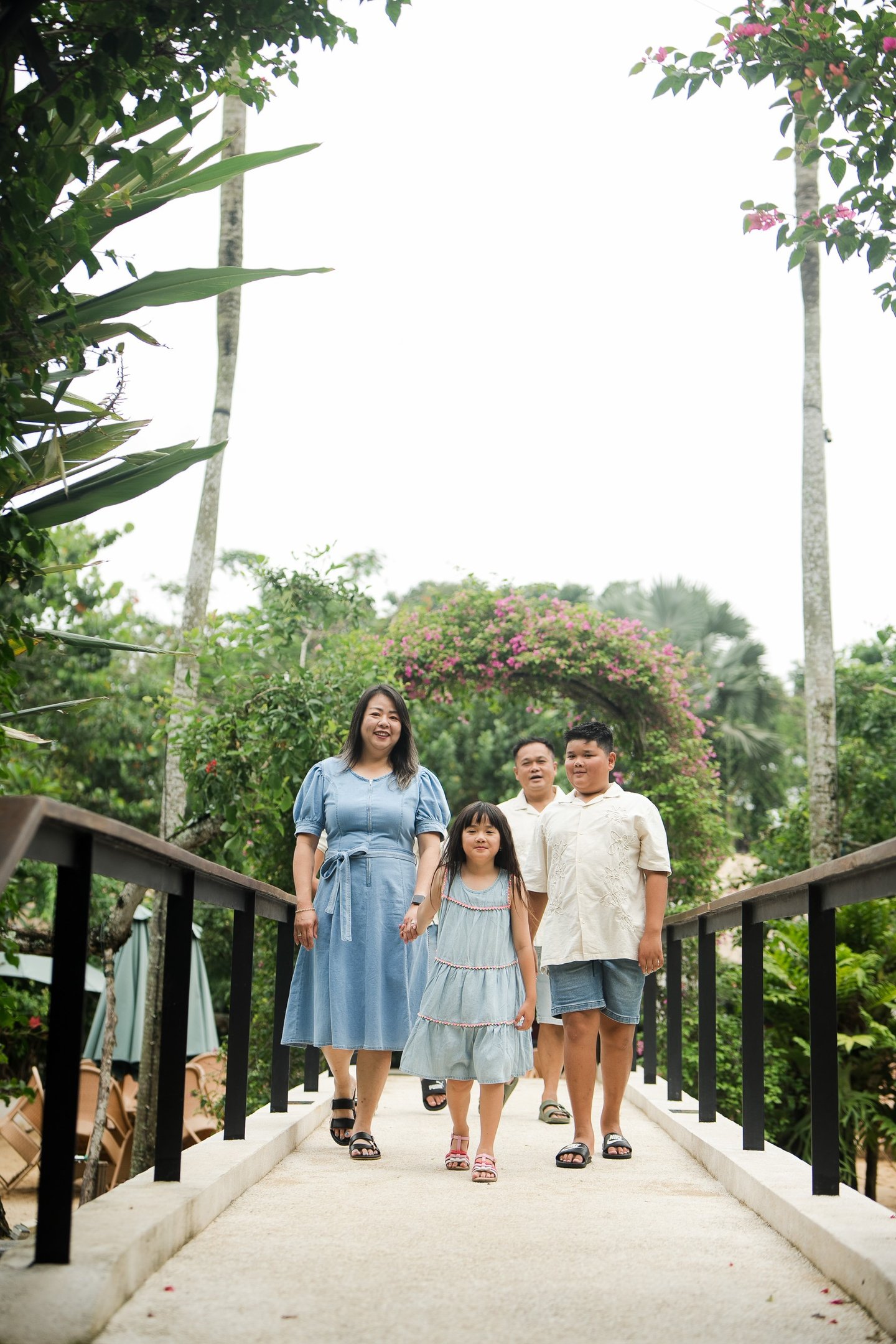 family walking together across a garden bridge during a natural family photography session at Movenpick Jimbaran Bali