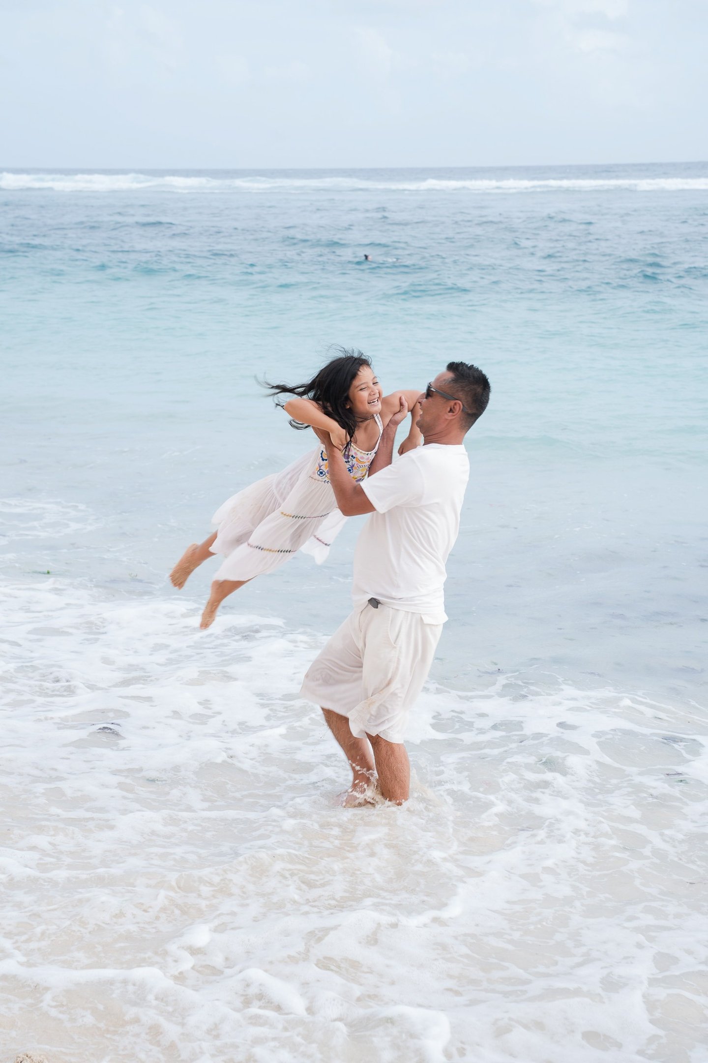 Father lifting daughter playfully in the ocean at Karma Kandara Bali  