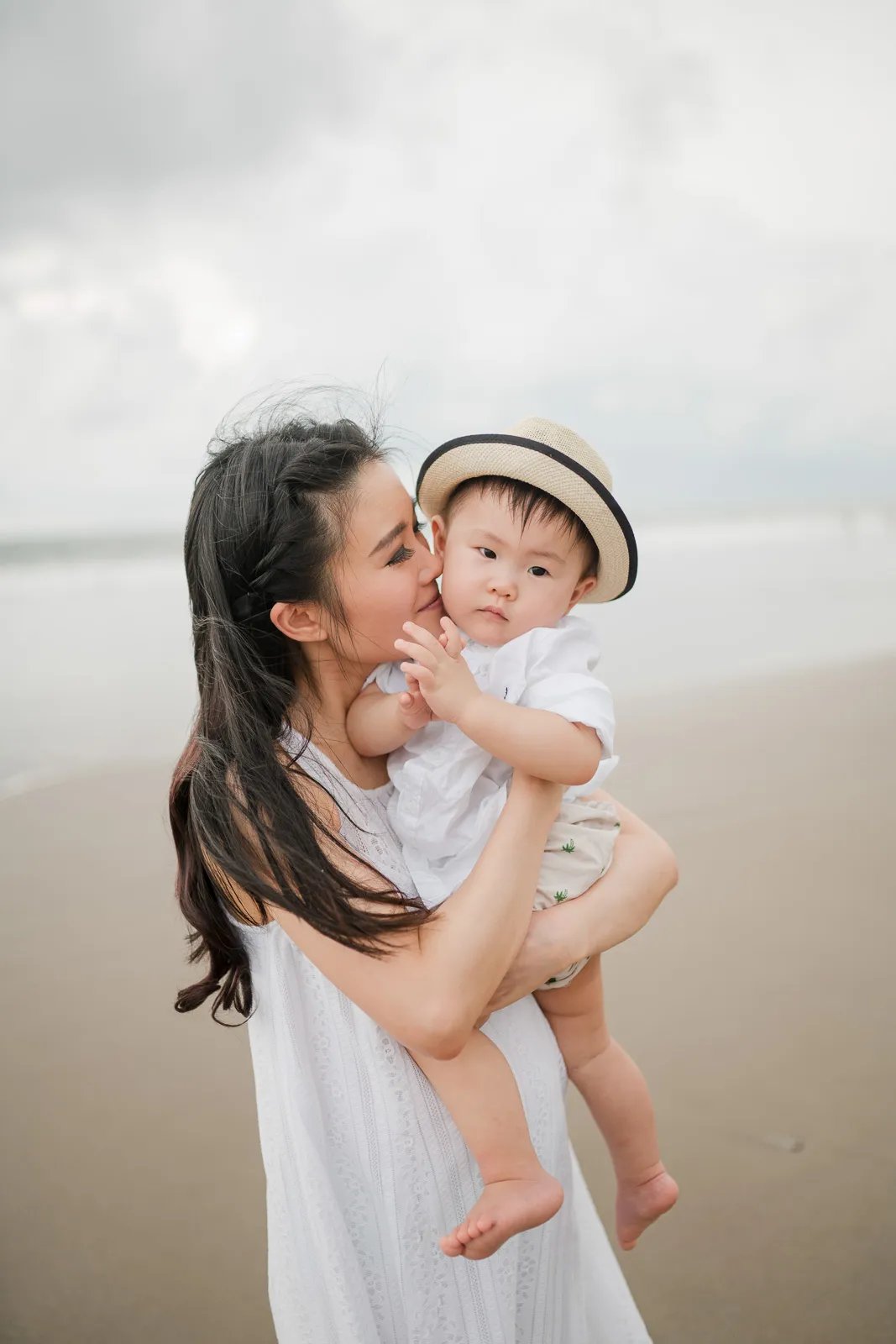 Mother holding baby during family photography session at Alila Seminyak Bali with calm beach atmosphere.