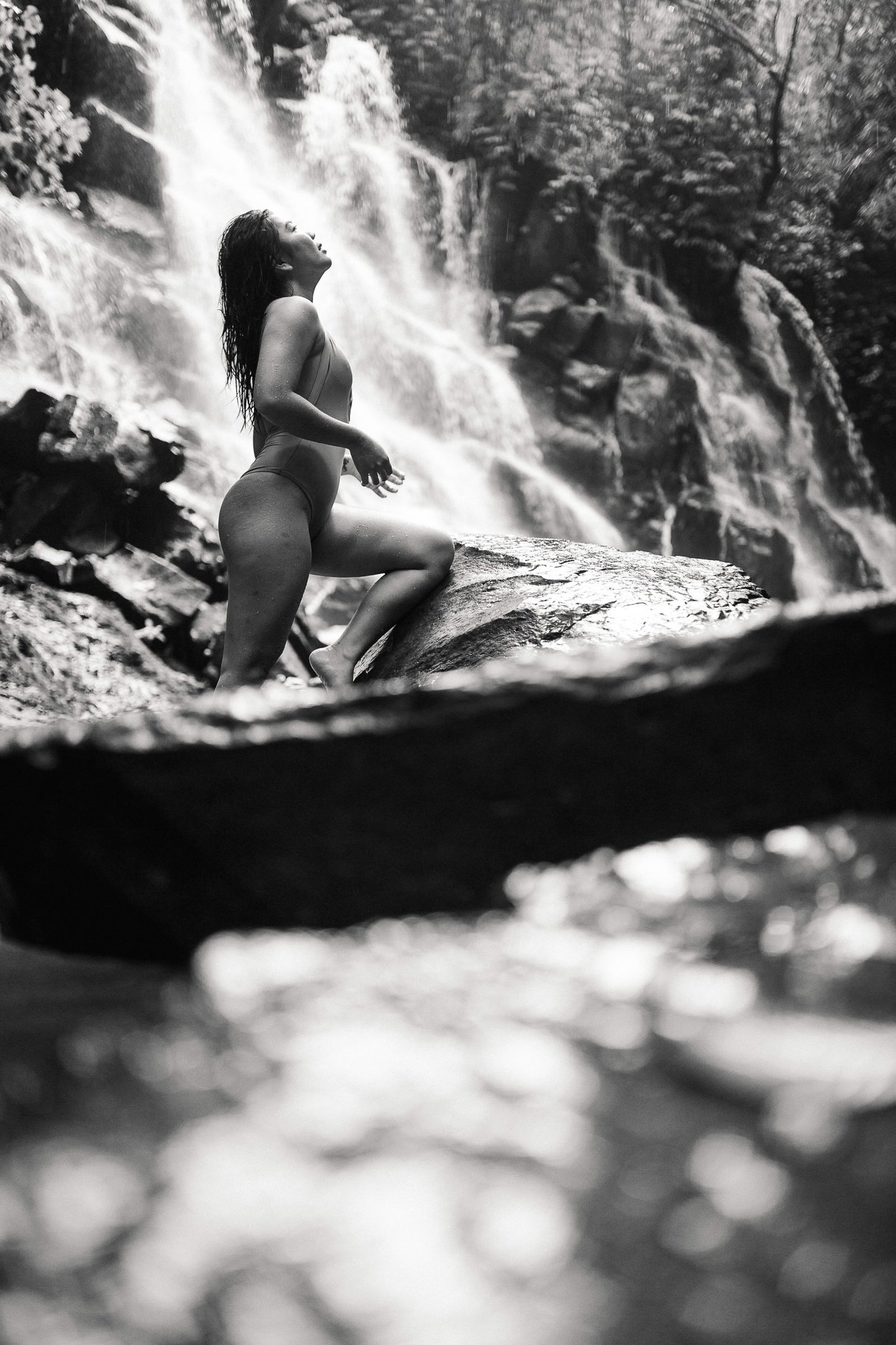 Black and white portrait of woman standing near waterfall rocks at Kanto Lampo Bali